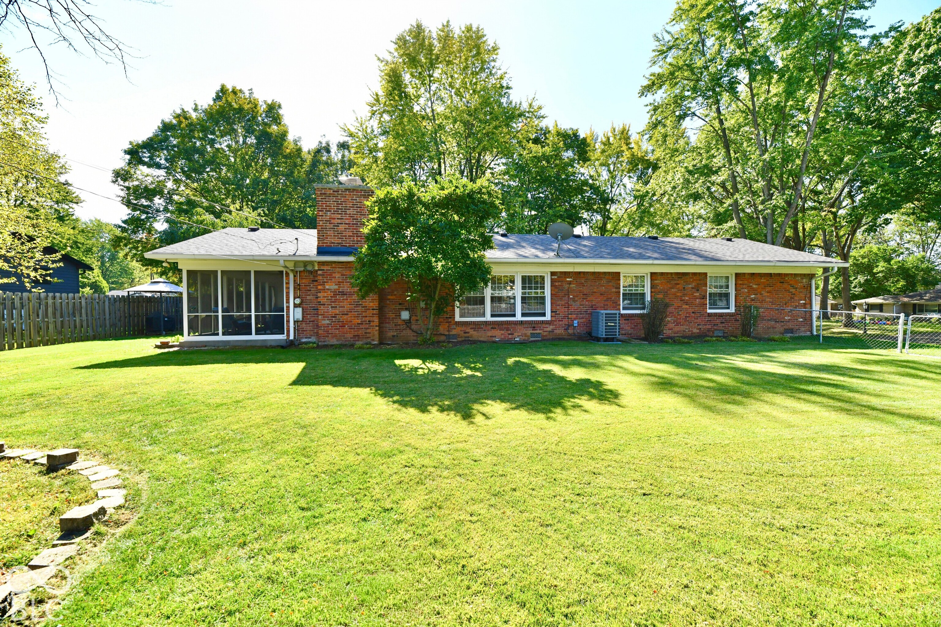 Exterior brick facade featuring a screened-in porch, masonry chimney, expansive lawn, and partial wood fencing