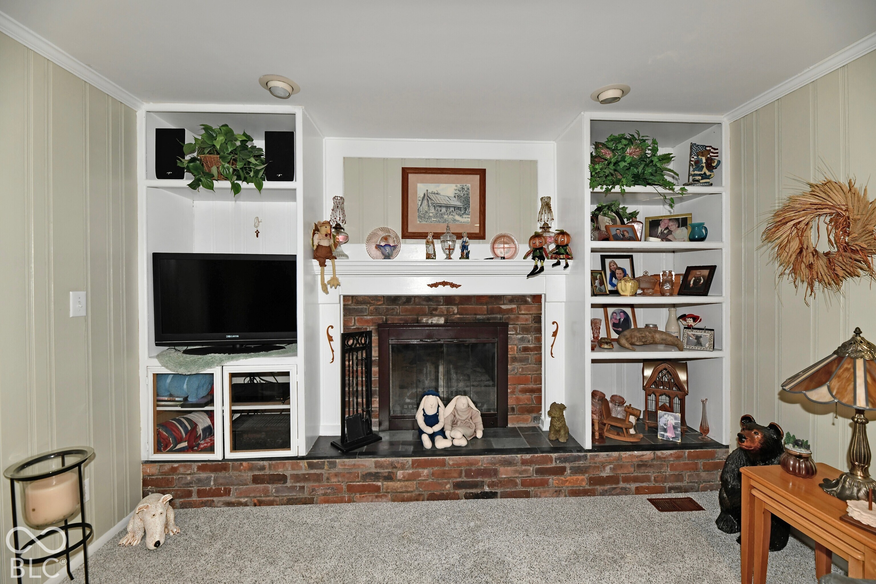 Brick fireplace featuring a raised hearth, white mantel, and integrated floor-to-ceiling built-in cabinetry with shelving