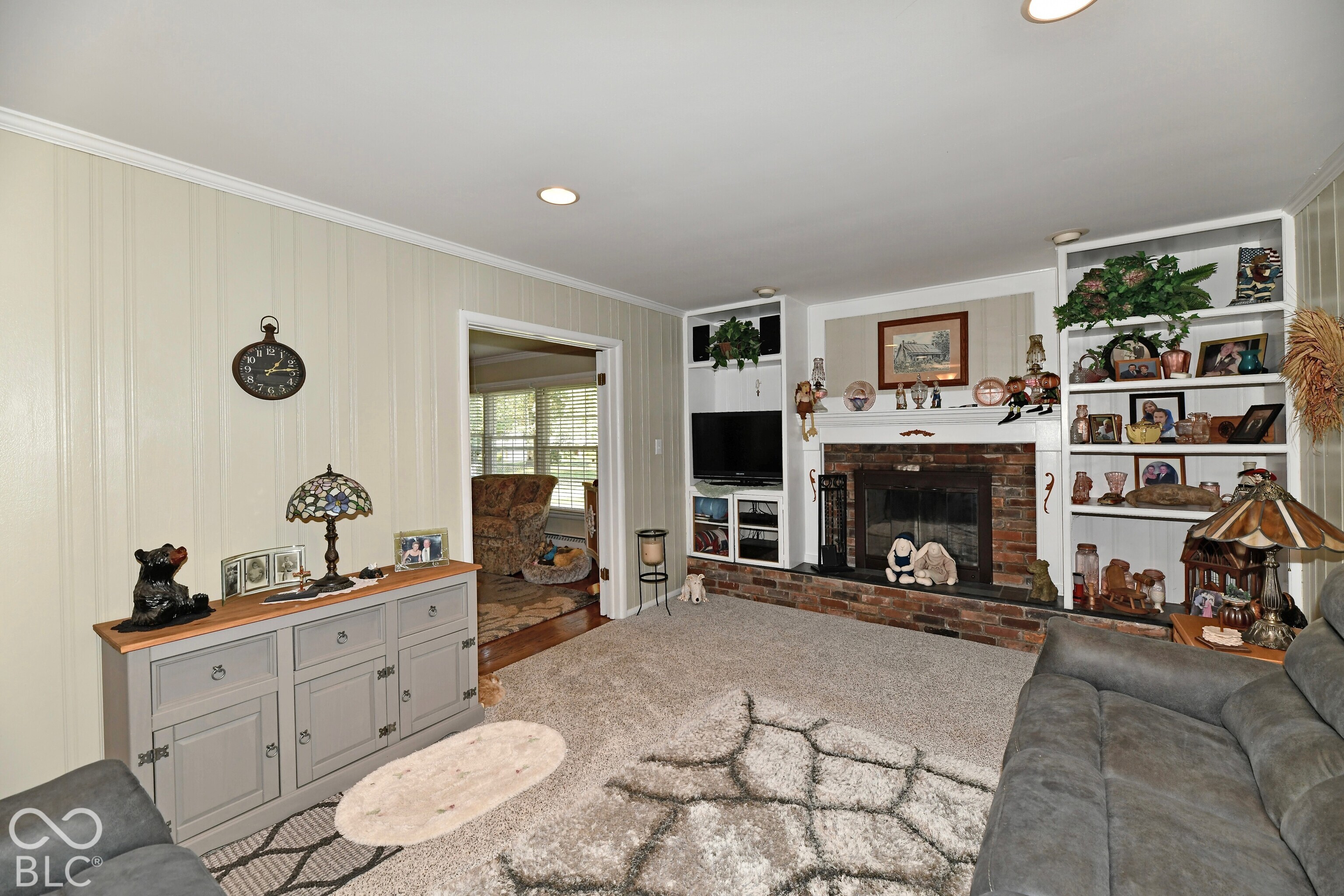 Interior space featuring a brick-surround fireplace, built-in floor-to-ceiling shelving, recessed lighting, and vertical paneled wall detailing