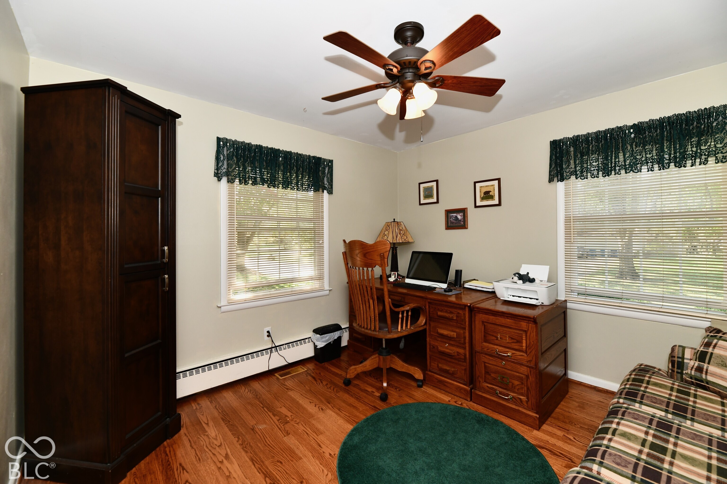 Room featuring wood-finish flooring, dual windows with integrated blinds, and a multi-blade ceiling fan with a three-light fixture