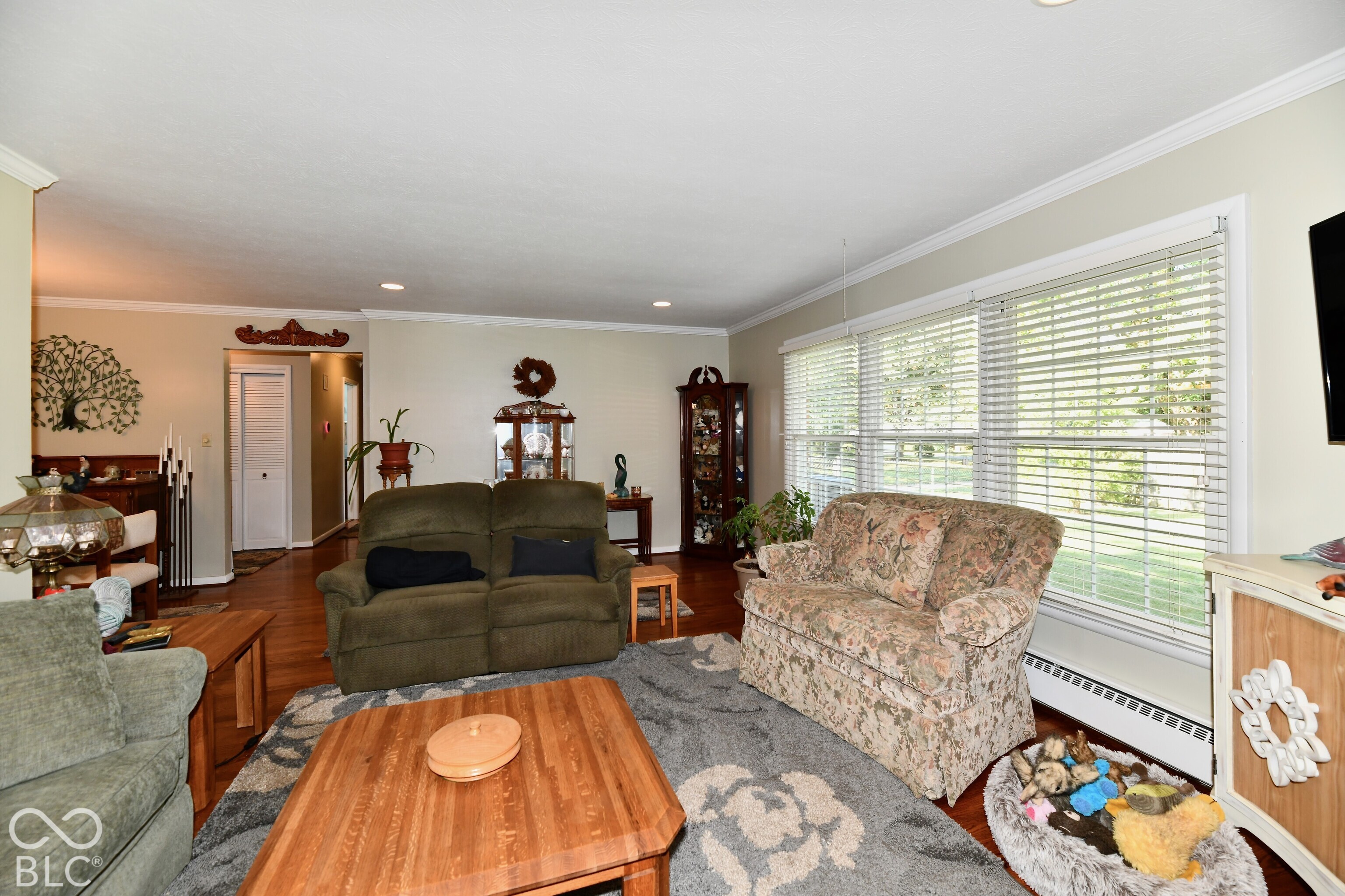 Living area featuring neutral wall tones, recessed lighting, crown molding, and large windows with horizontal blinds