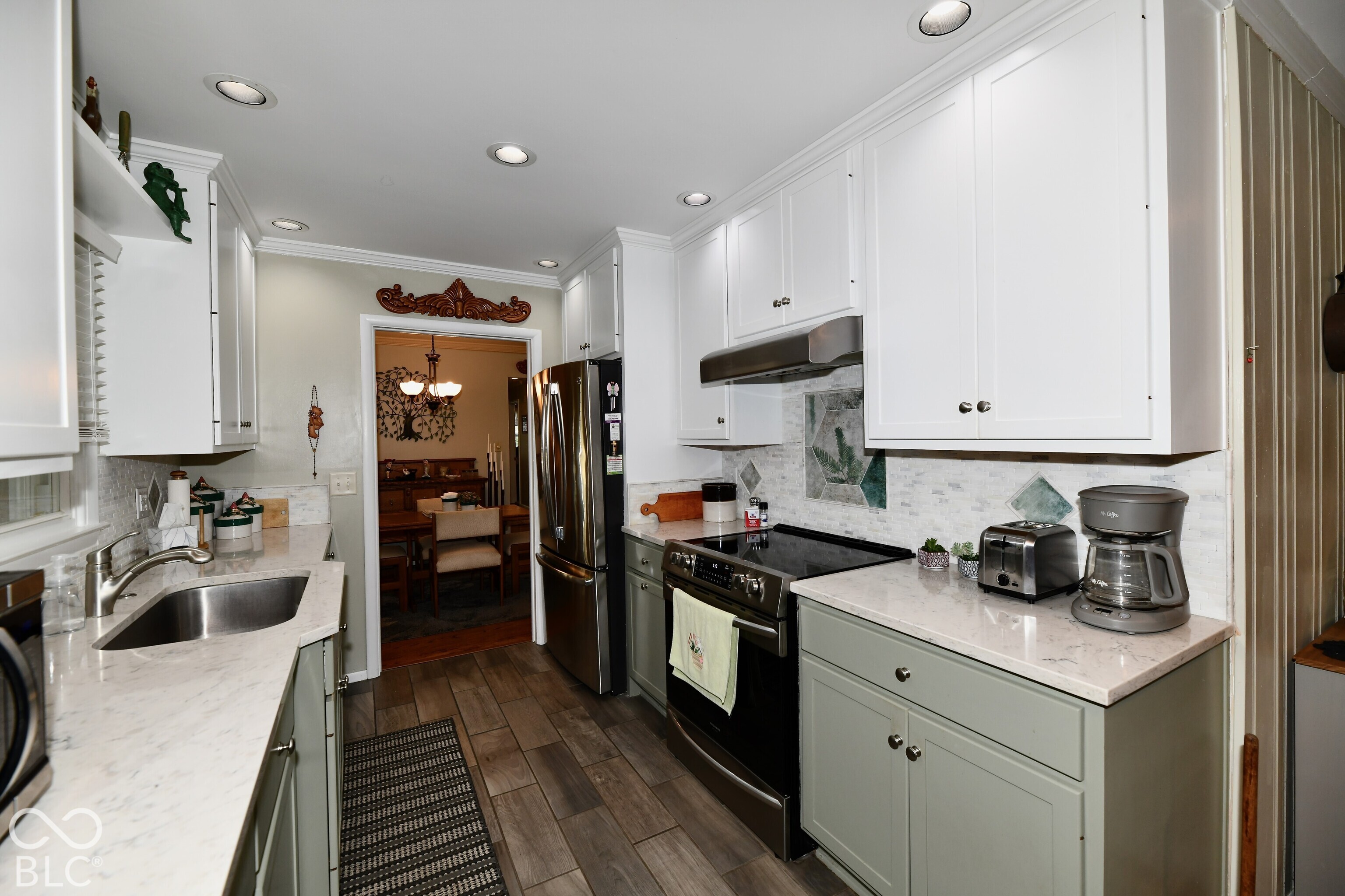 Kitchen featuring white upper cabinetry, sage green lower cabinetry, stone-finish countertops, stainless steel appliances, and wood-finish flooring