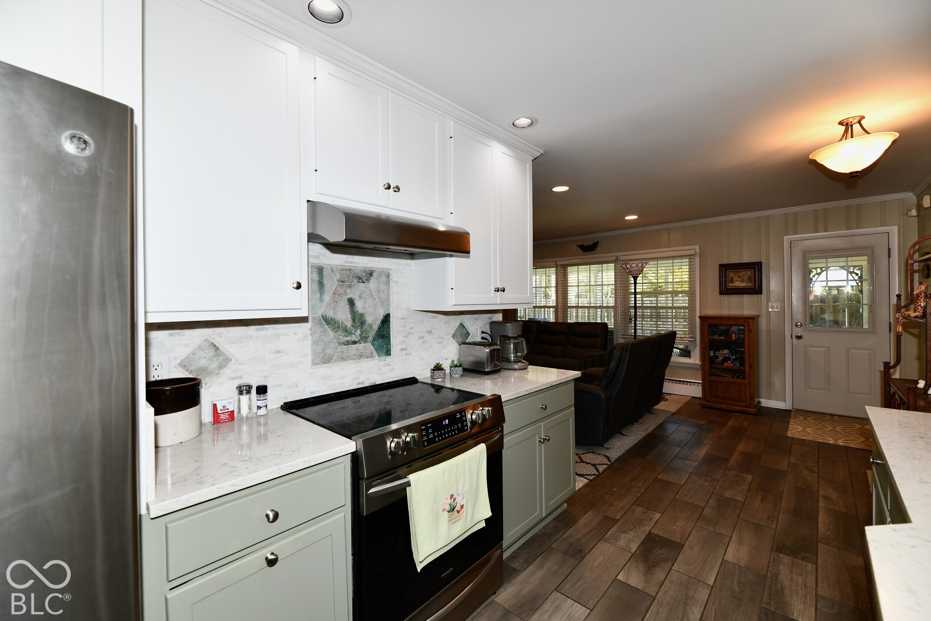 Kitchen featuring custom white upper and sage green lower cabinetry, quartz countertops, a decorative tile backsplash, stainless steel range with overhead vent, and wood-finish flooring