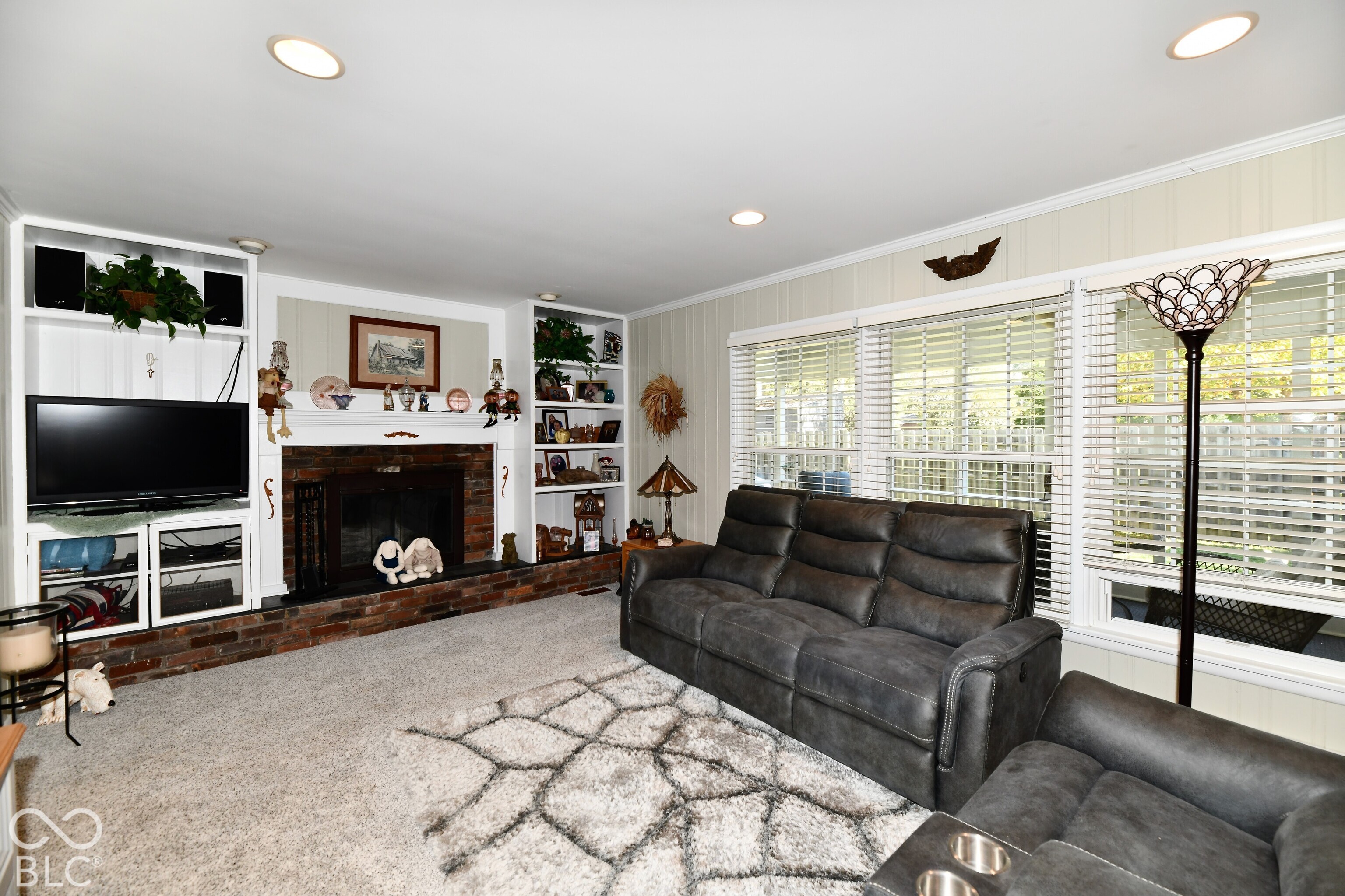 Brick-faced fireplace with white built-in shelving, recessed ceiling lighting, and multi-pane windows