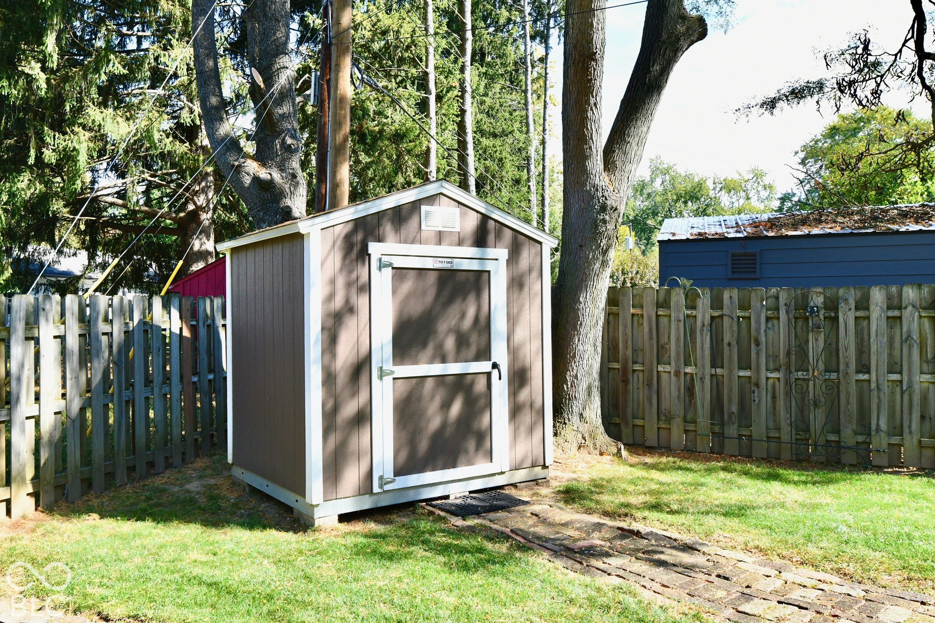 Detached storage structure featuring vertical siding, white trim, a gabled roof, and a stone paver path