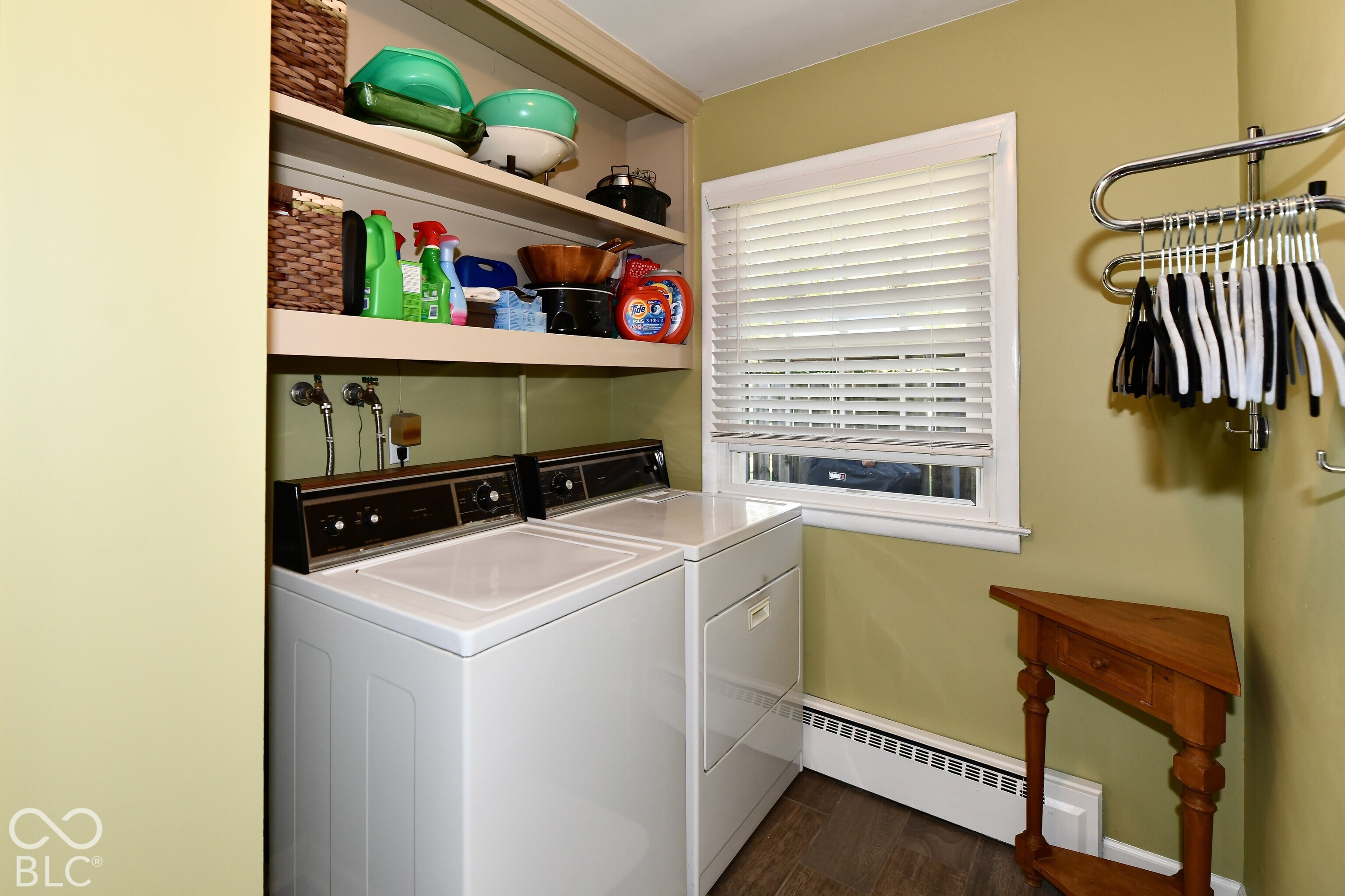 Laundry area featuring built-in overhead cabinetry, wood-finish flooring, a window with horizontal blinds, and a wall-mounted garment rack