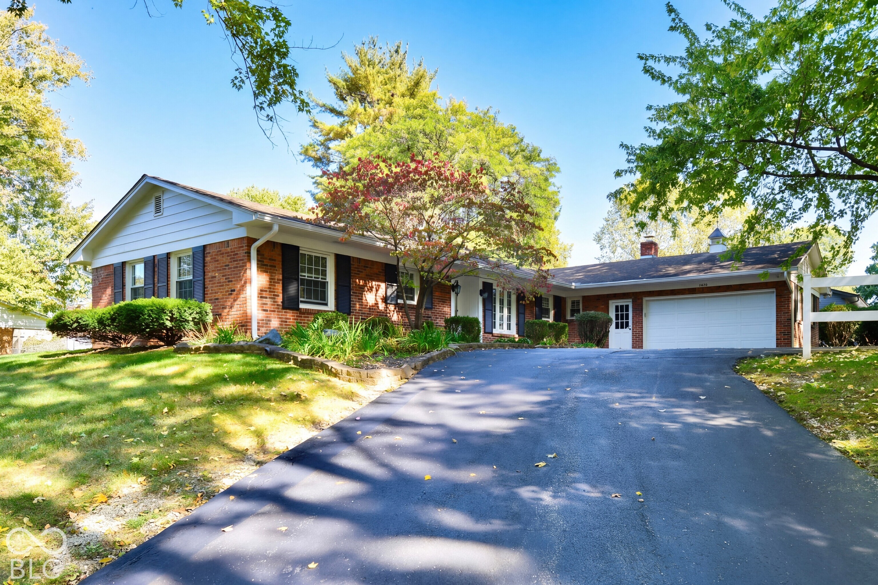 Ranch-style residence featuring a classic brick and white horizontal siding exterior, attached multi-car garage, asphalt driveway, and landscaped front grounds with mature trees