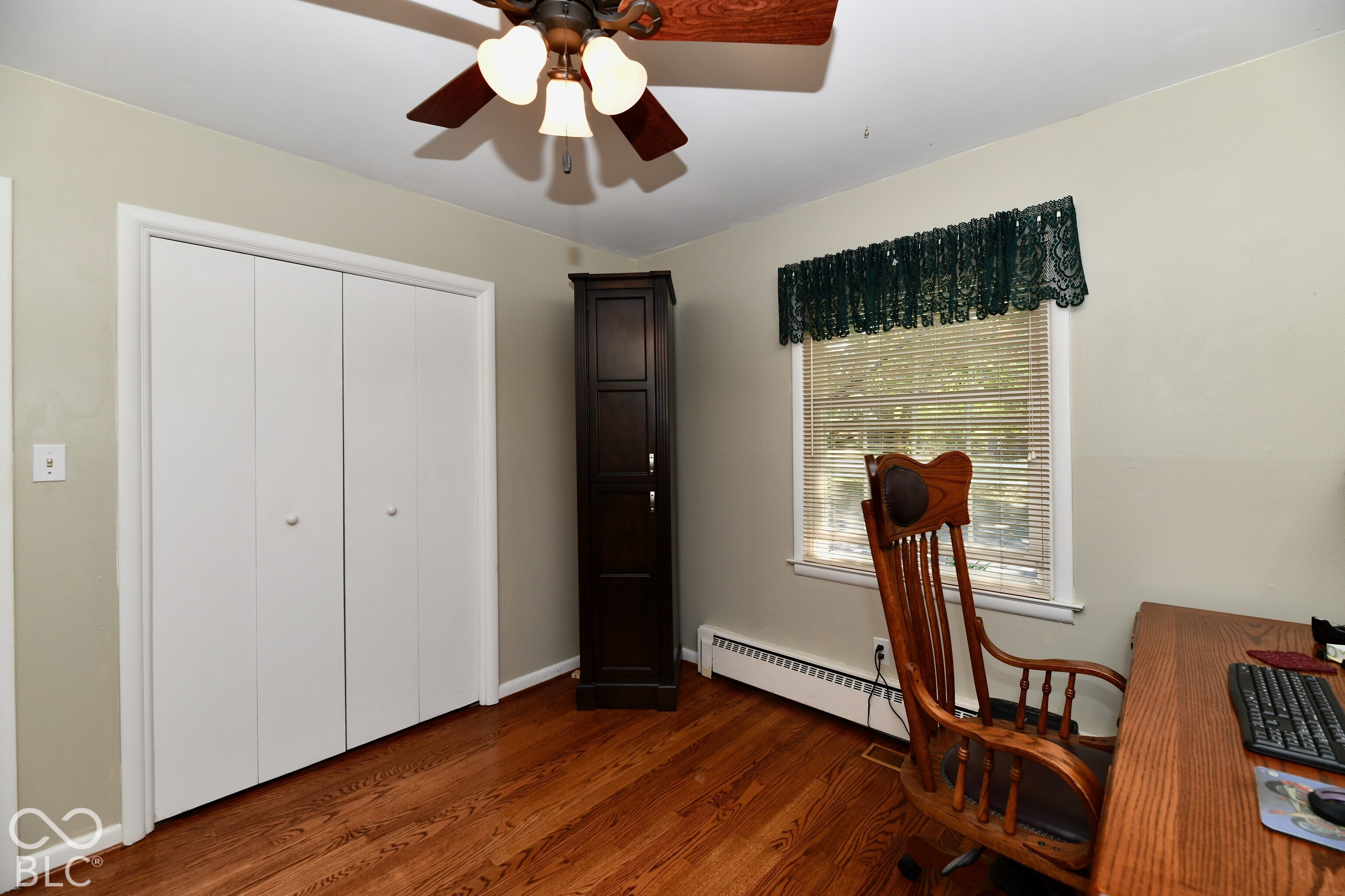 Room featuring wood-finish flooring, a built-in dark wood cabinetry unit, a double-door closet, and a ceiling fan with integrated lighting