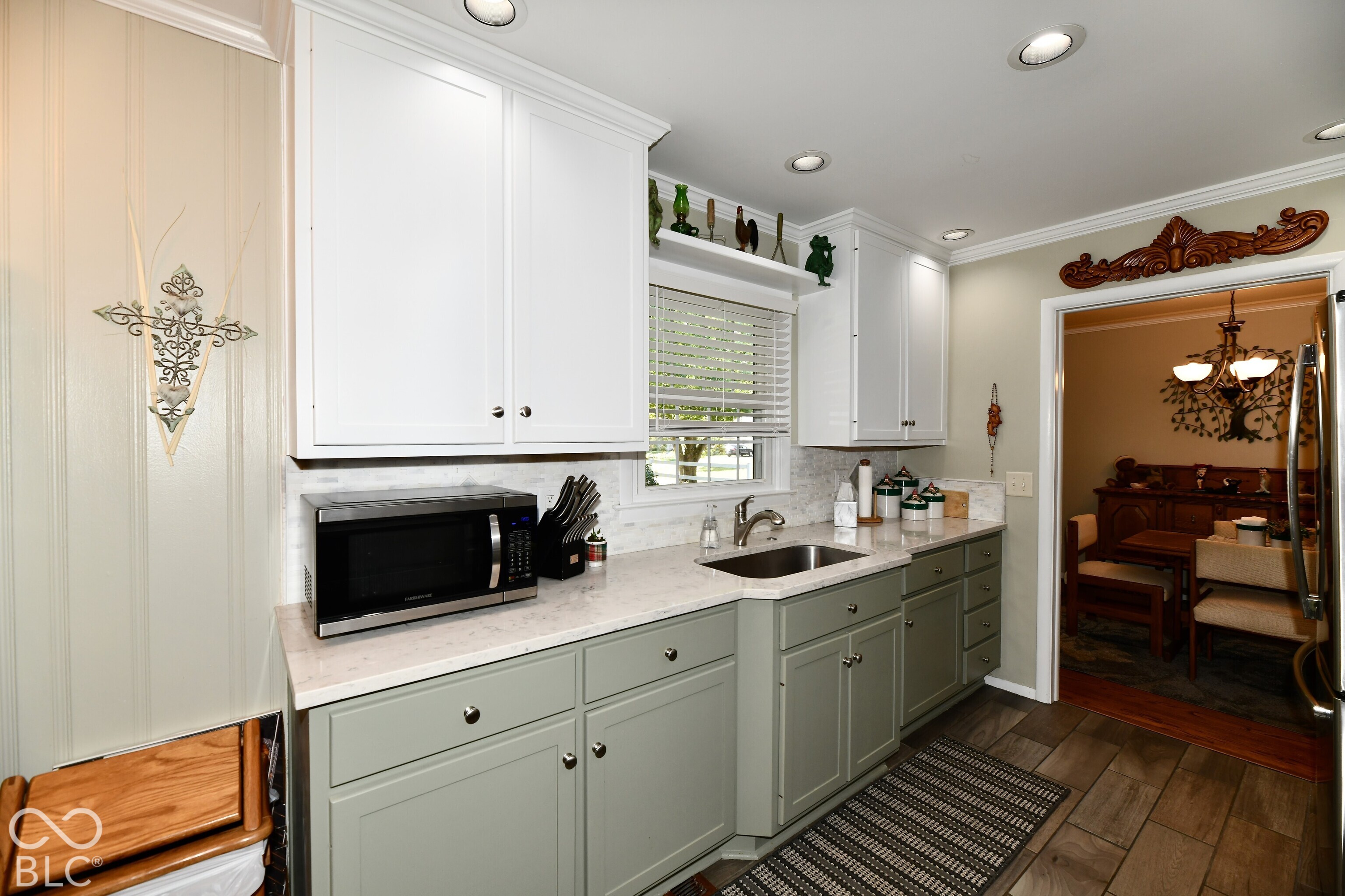 Kitchen featuring two-tone shaker-style cabinetry, light-toned stone-finish countertops, subway tile backsplash, stainless steel undermount sink, and wood-finish flooring
