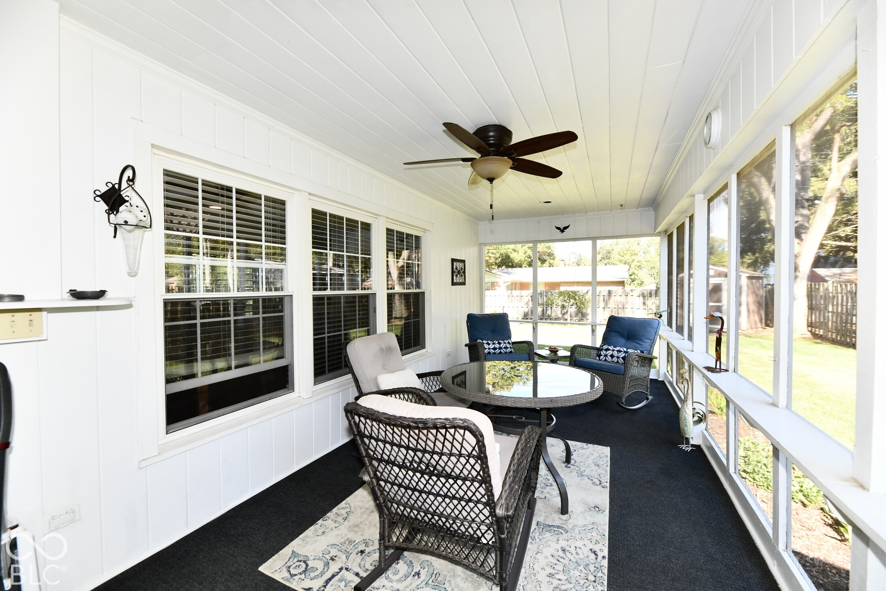 Enclosed porch featuring white paneled walls, floor-to-ceiling window walls, dark carpeting, and a ceiling-mounted fan