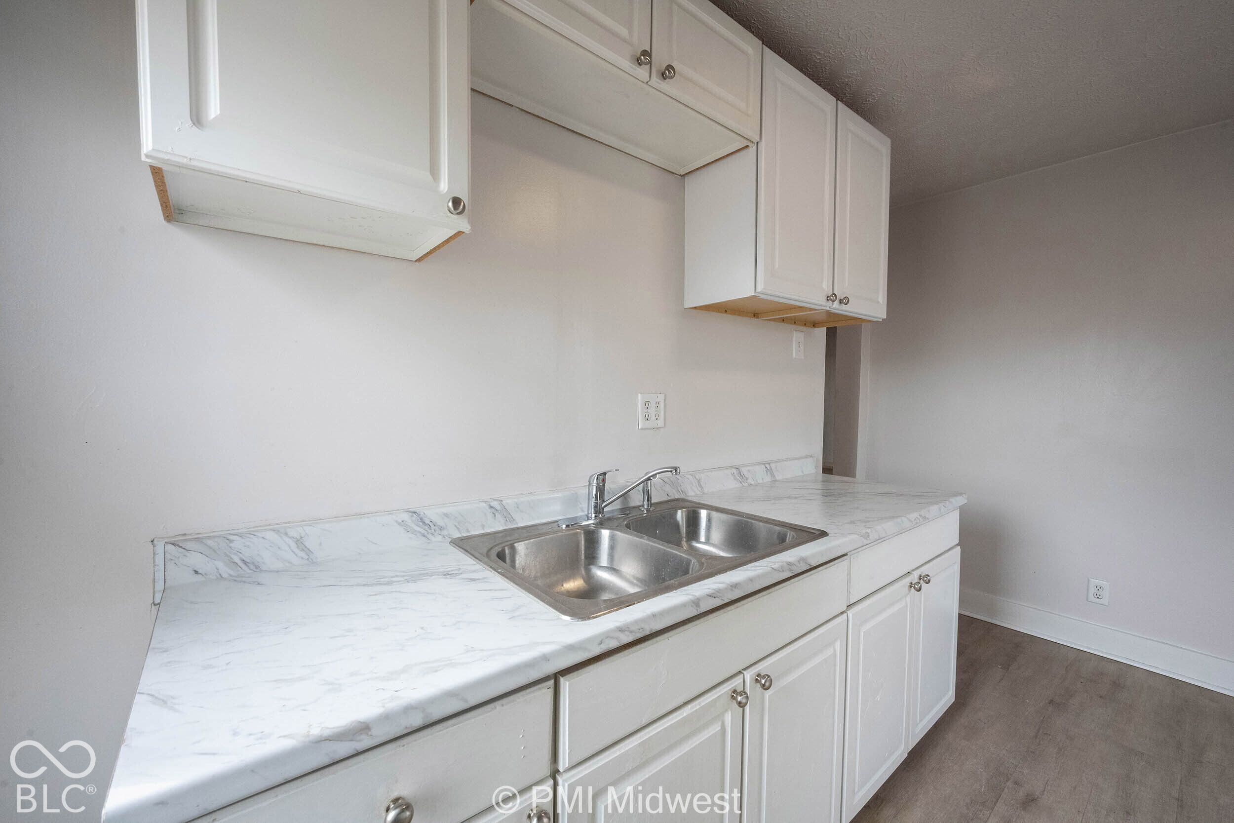 White cabinetry, double-basin stainless steel sink, chrome faucet, stone-finish laminate countertop, and wood-finish flooring