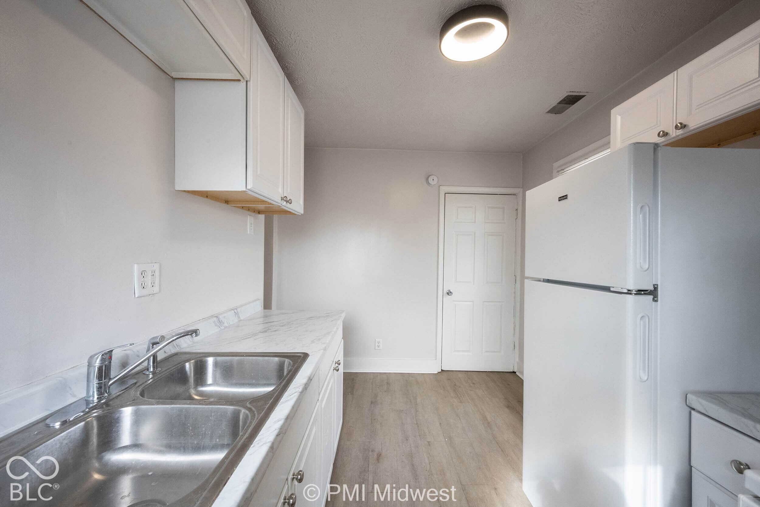 Kitchen featuring white cabinetry, stone-patterned countertops, a double-basin stainless steel sink with a high-arch faucet, and wood-finish flooring