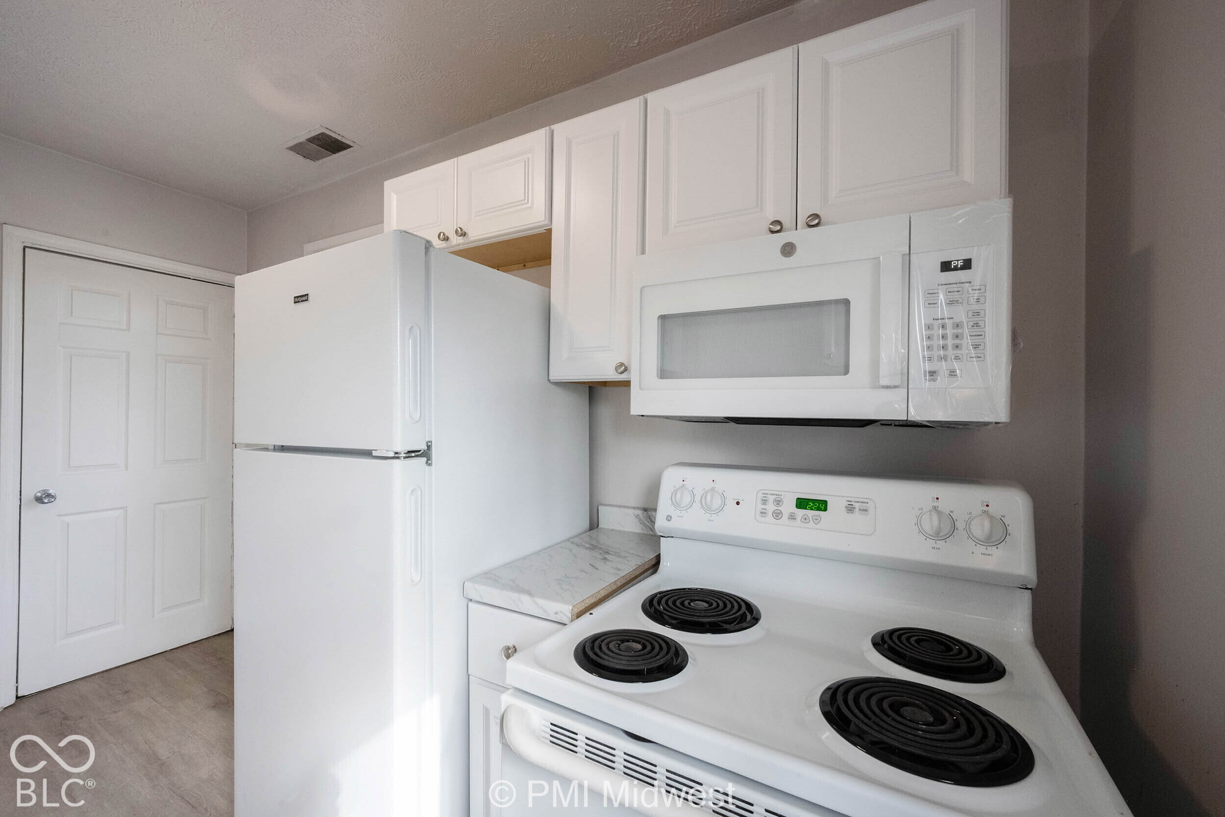 Kitchen featuring white cabinetry, integrated white microwave, four-burner electric range, top-freezer refrigerator, and stone-finish laminate countertops