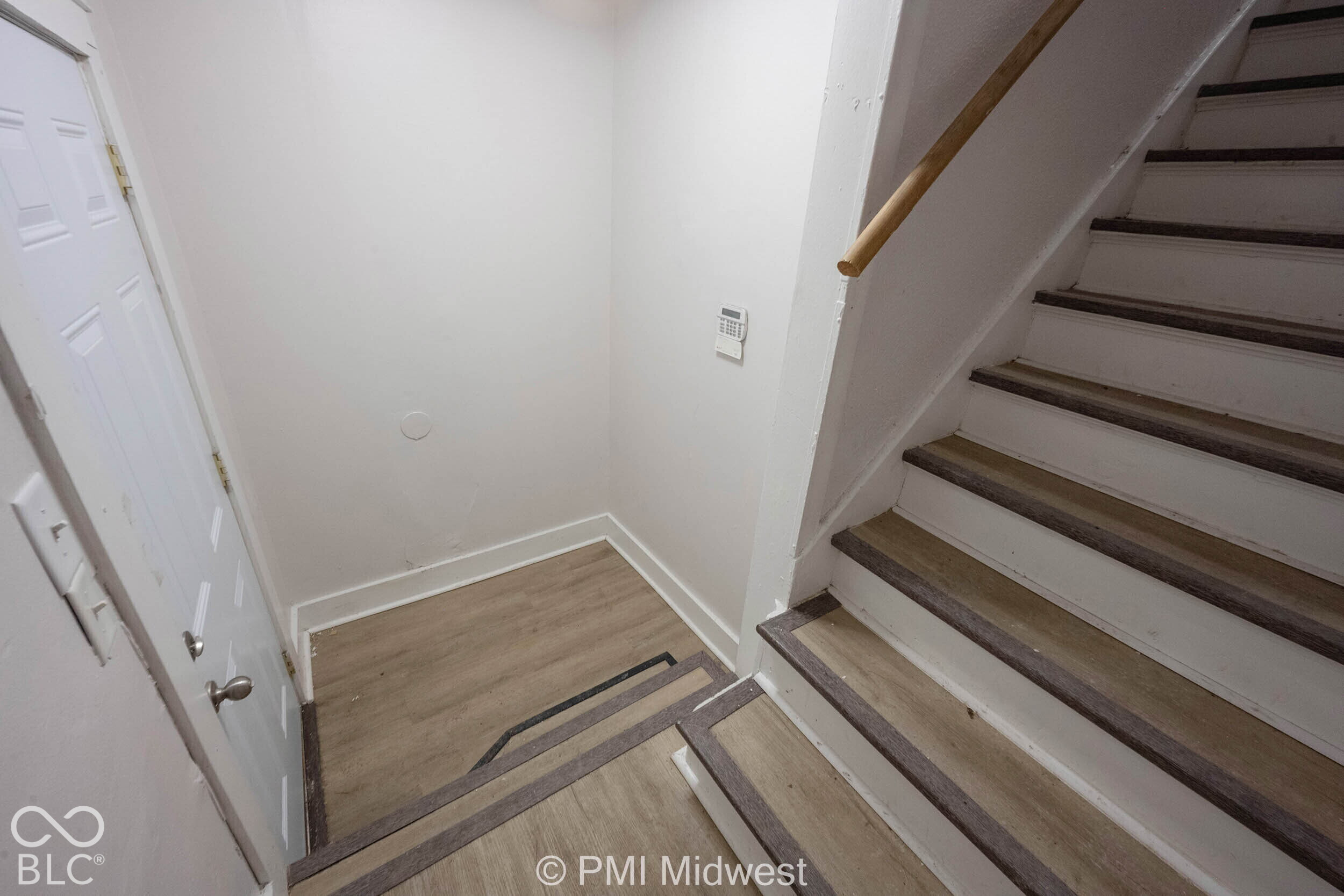 Interior staircase featuring wood-finish treads with dark trim, neutral-toned wood-finish flooring, and a natural wood handrail