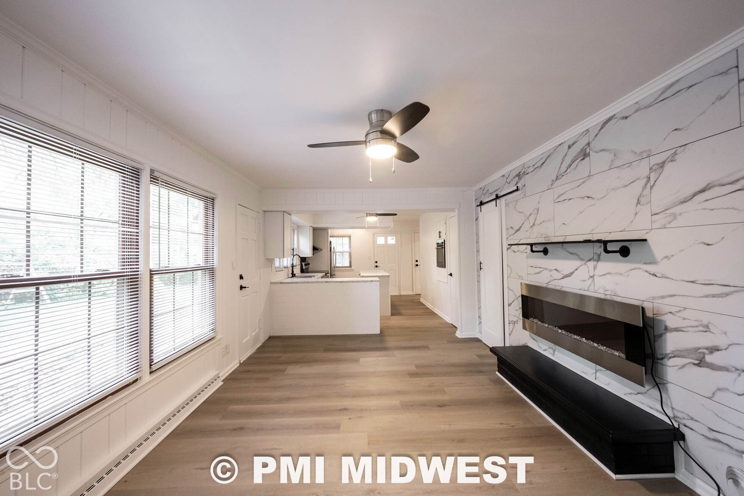 Living space featuring wood-finish flooring, stone-patterned wall tile, a wall-mounted electric fireplace, and a three-blade ceiling fan