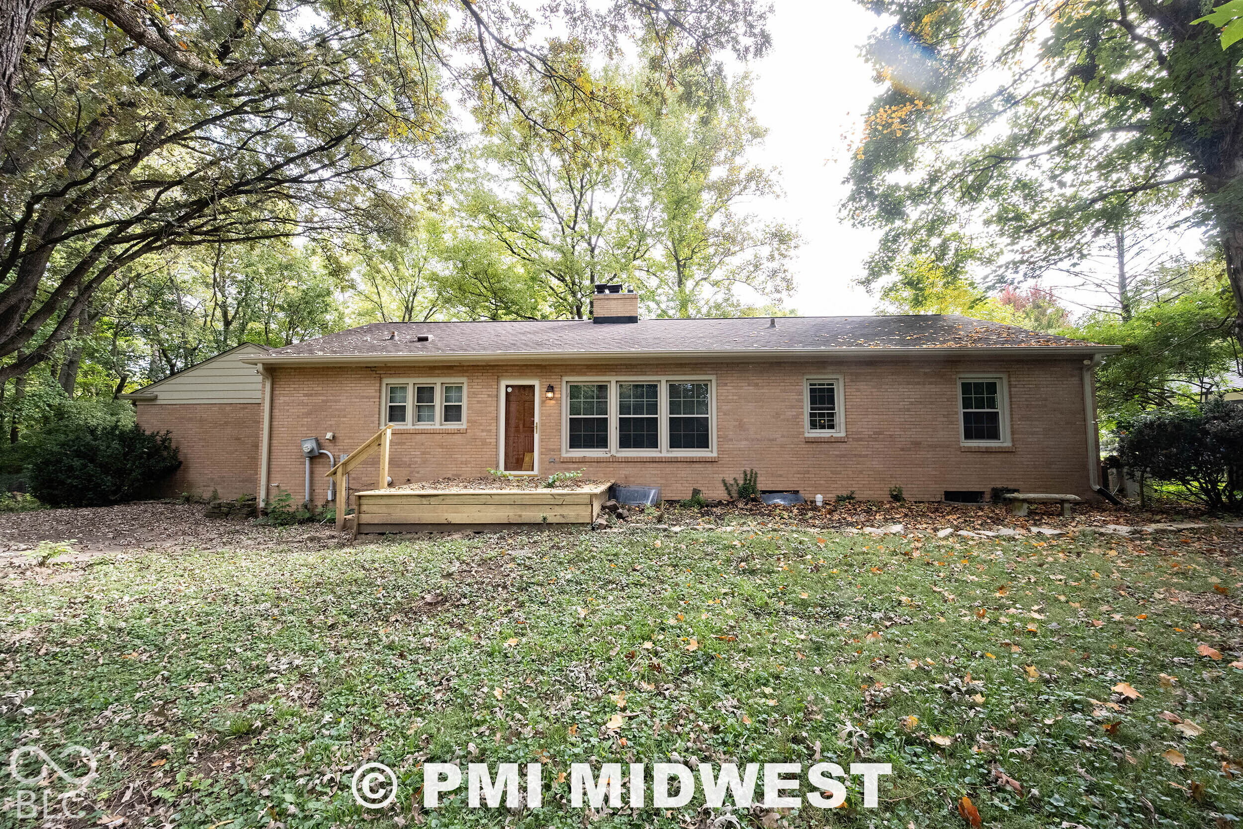Brick exterior residence featuring a wooden deck, a chimney, and mature trees on the surrounding grounds