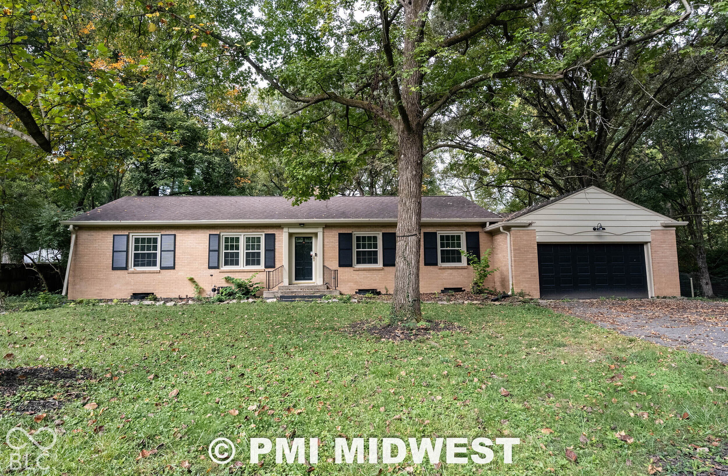 Single-story brick exterior featuring dark shutters, attached garage, and mature trees on the lot