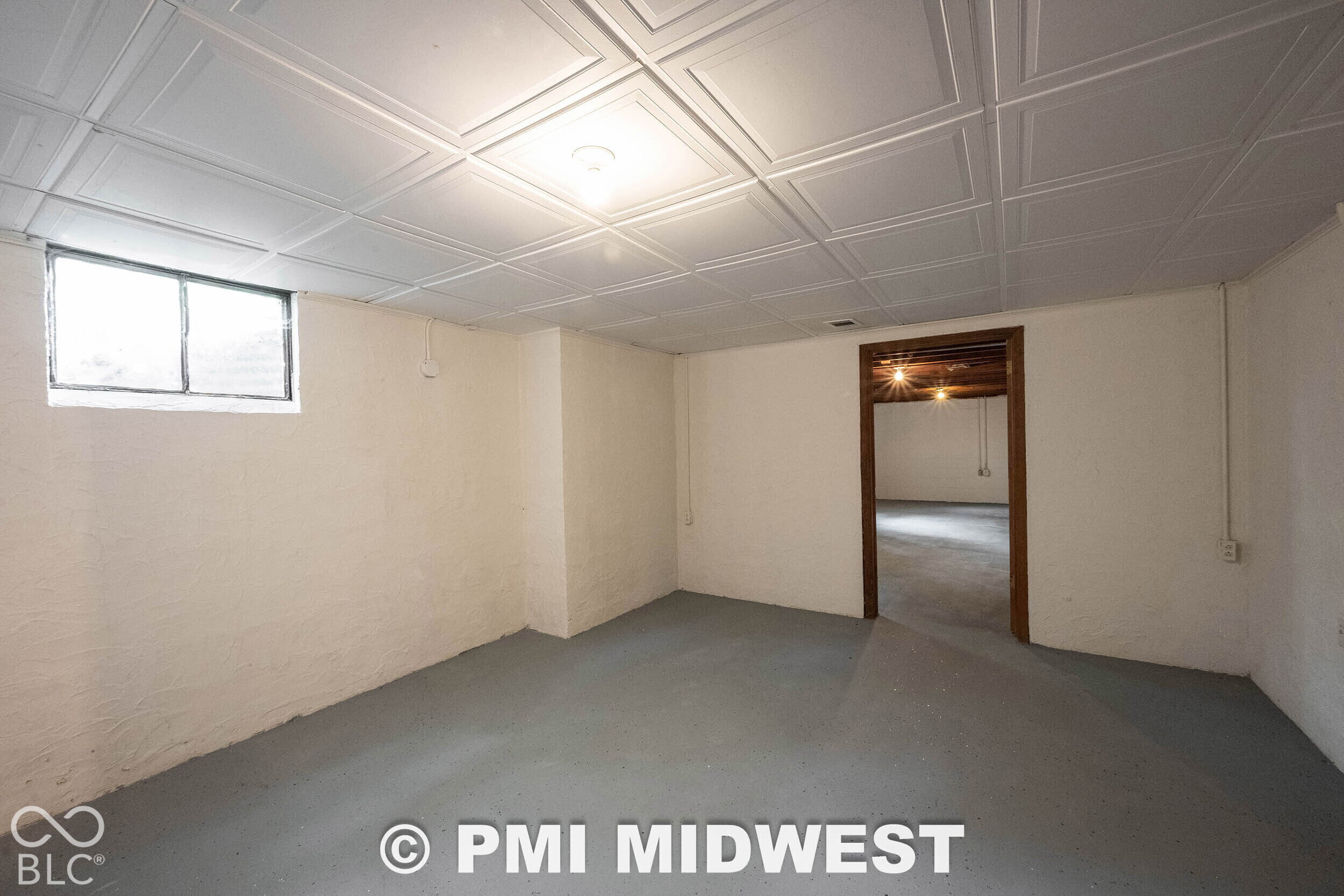 Finished space featuring a white coffered ceiling, painted concrete flooring, smooth masonry walls, and a recessed window