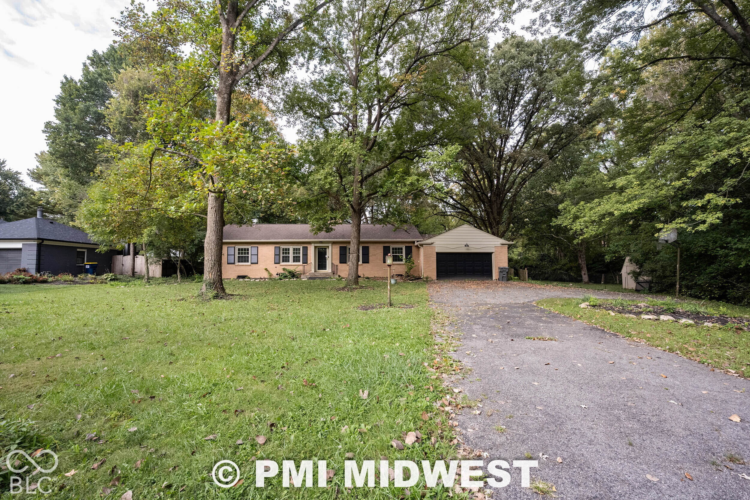 Single-story residence with a brick exterior, shutter-framed windows, attached garage, and mature trees on a spacious lot