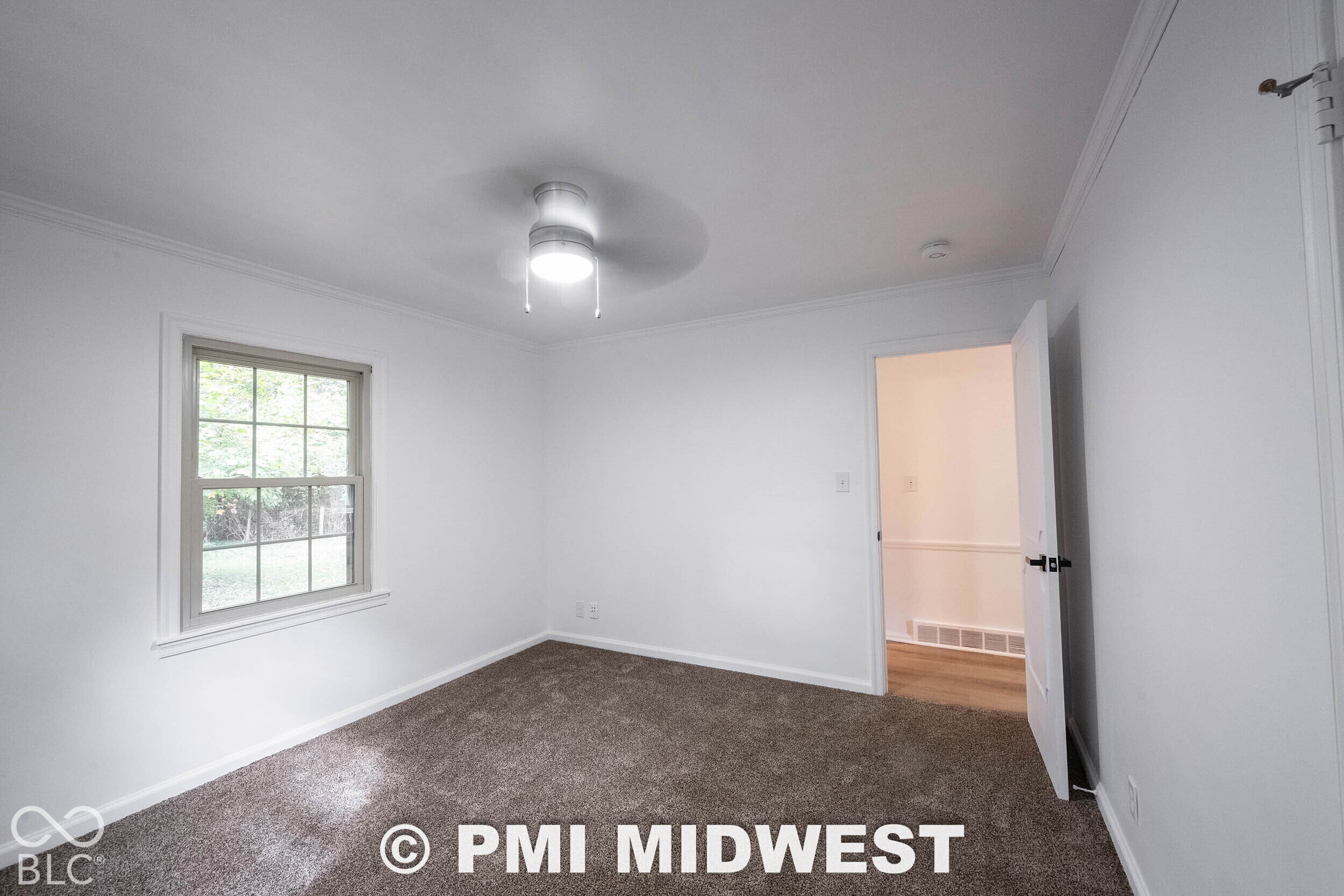 Room featuring neutral carpeting, multi-pane window, and a ceiling-mounted light fixture with integrated fan