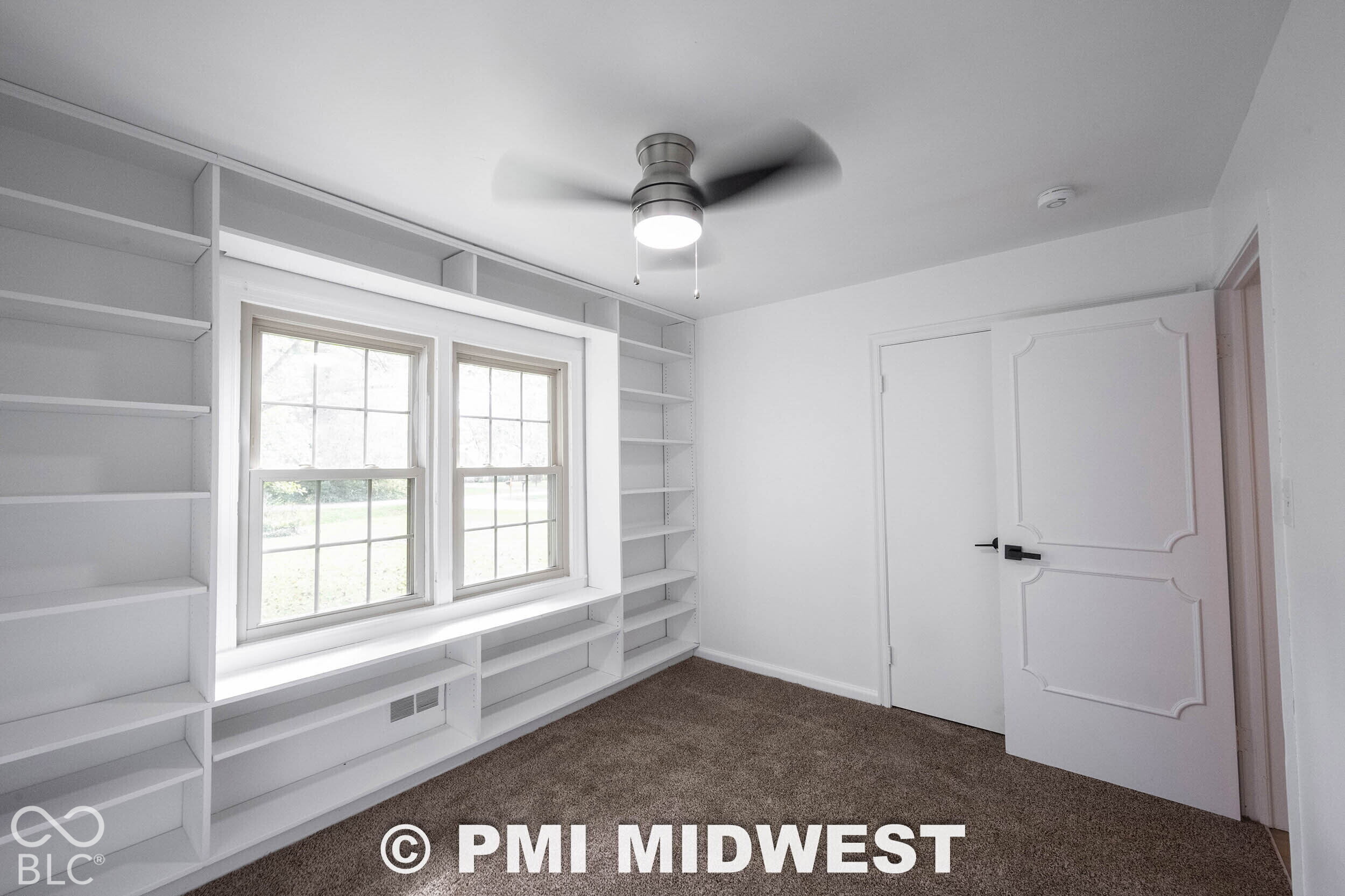 Built-in white floor-to-ceiling shelving, recessed window seat, multi-pane window, flush-mount ceiling fan with integrated lighting, and paneled interior door