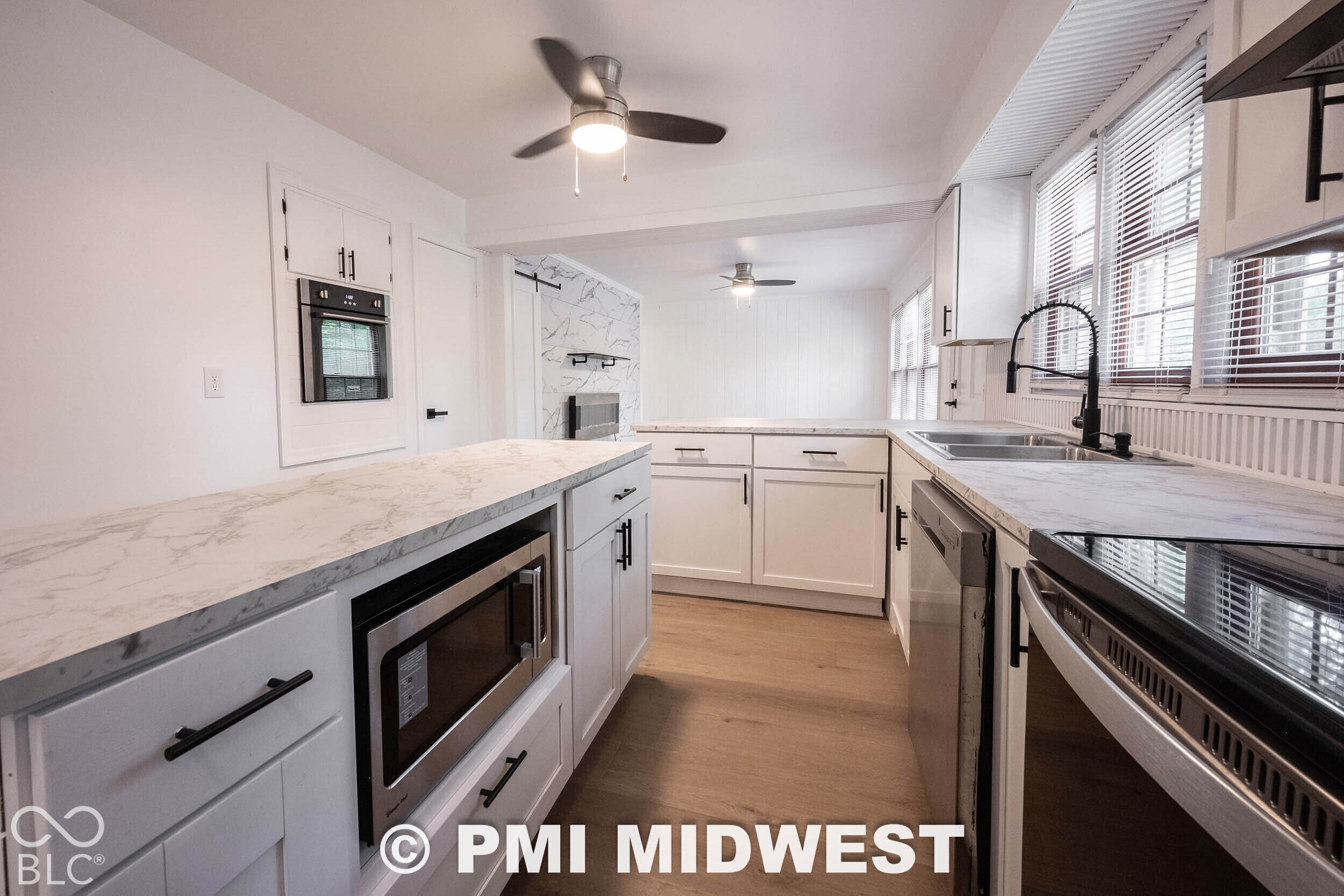 Kitchen featuring white cabinetry with matte black hardware, stone-patterned countertops, wood-finish flooring, built-in wall oven, and a gooseneck faucet