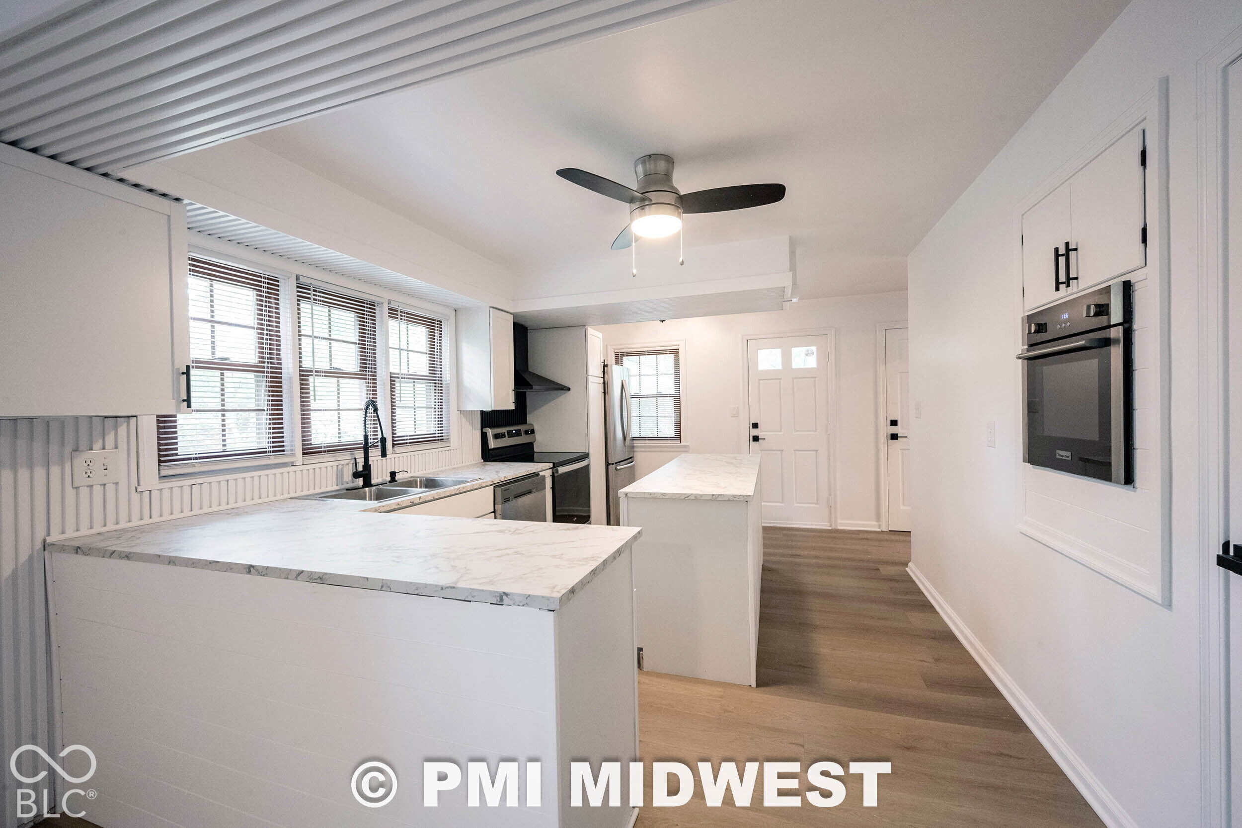 Kitchen featuring white cabinetry with matte black hardware, stone-patterned countertops, wood-finish flooring, a built-in wall oven, and a ceiling fan with integrated lighting