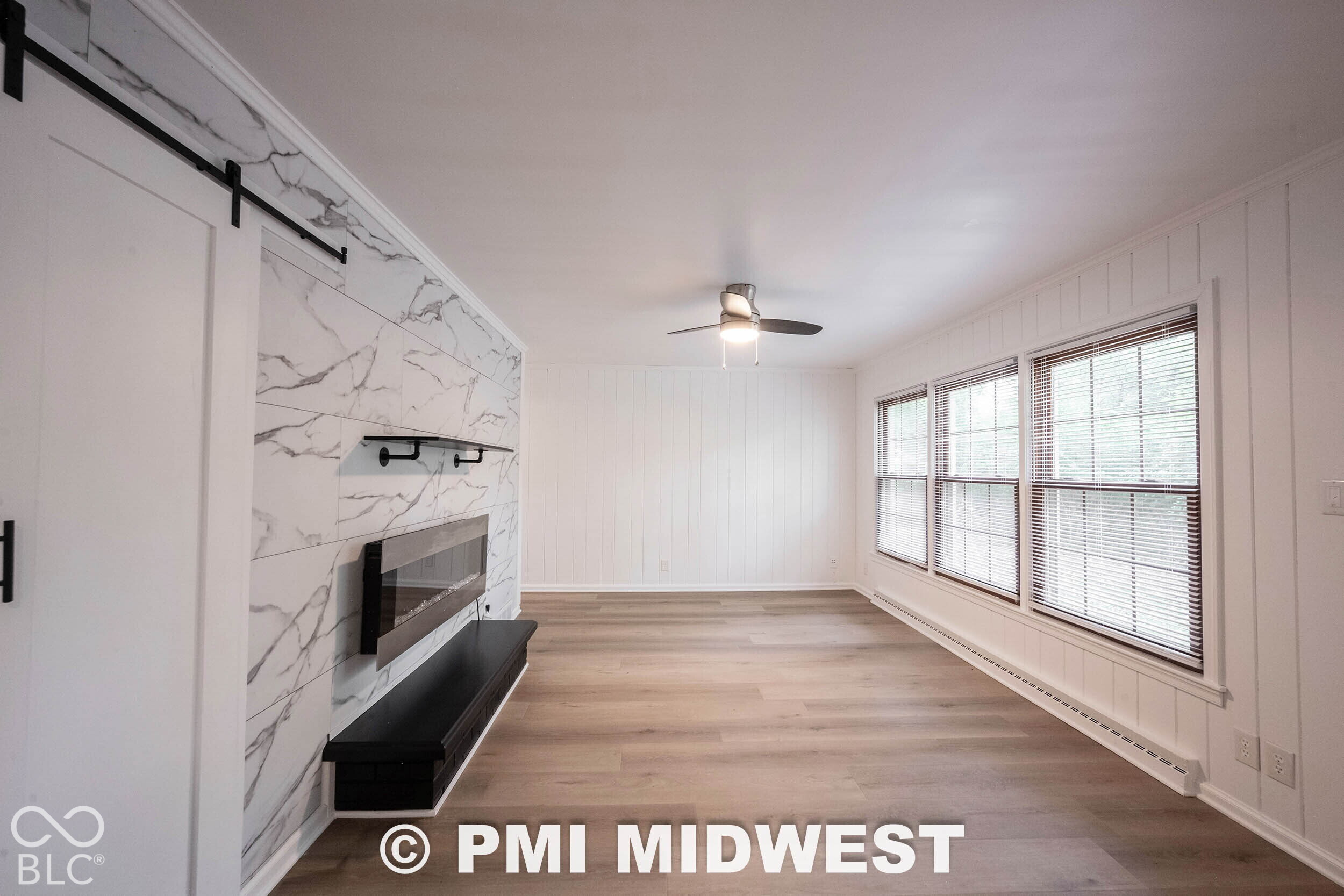 Stone-patterned accent wall featuring a black built-in fireplace, white vertical wall paneling, wood-finish flooring, and a ceiling fan with integrated lighting
