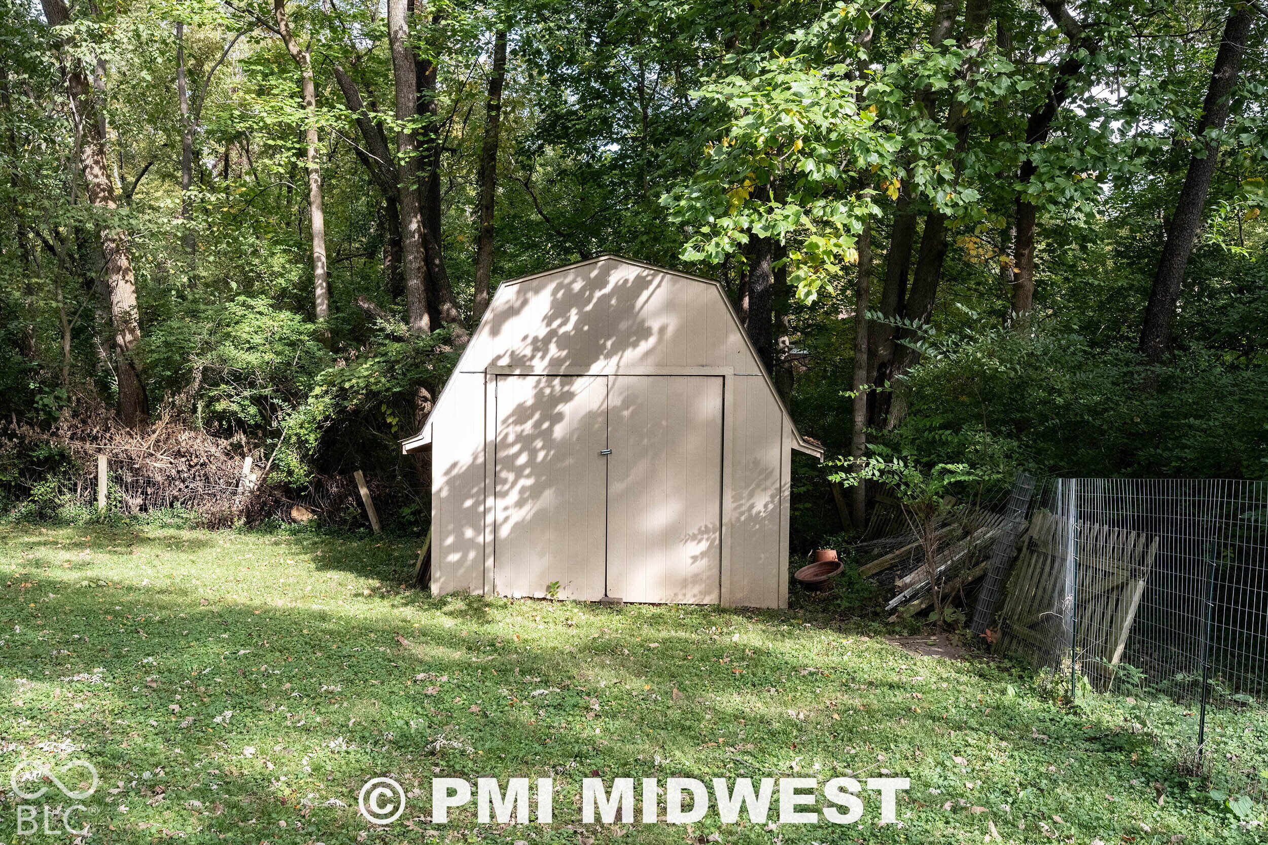 Exterior storage shed with a gambrel roof design, double-door entry, and wood-panel siding situated on a wooded lot