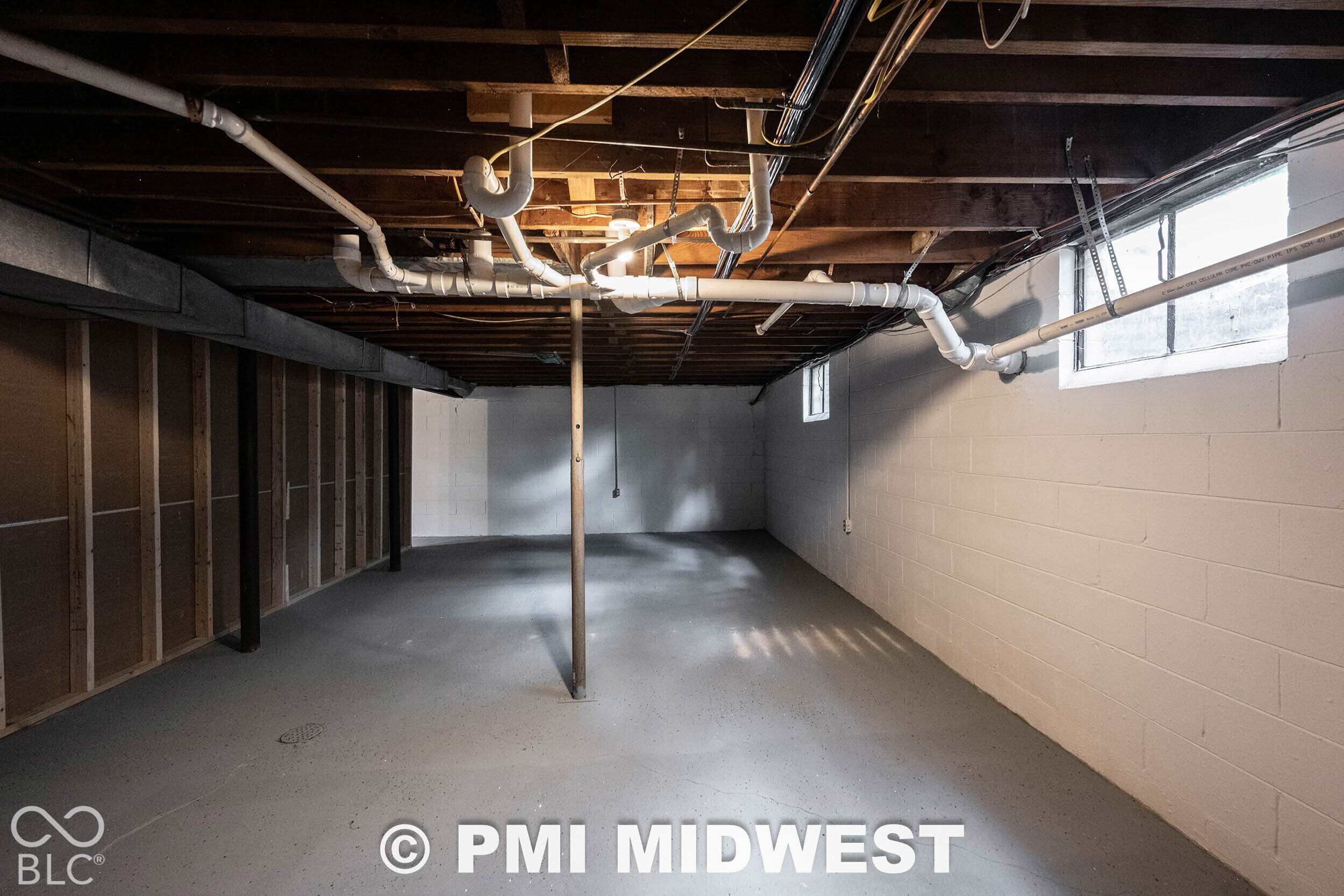 Lower-level area featuring painted concrete masonry unit walls, an exposed wood joist ceiling, painted concrete flooring, and multiple hopper-style windows