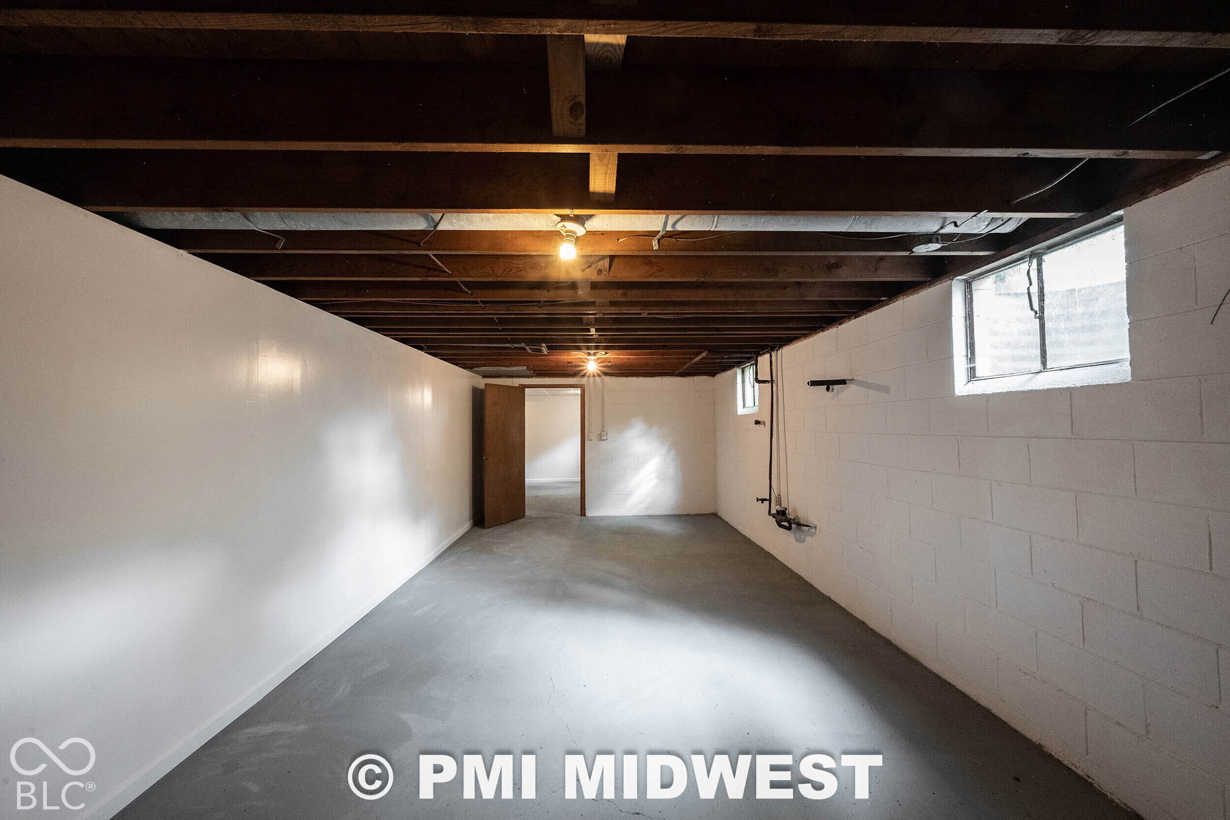 Unfinished lower level featuring exposed wood joist ceilings, painted concrete block walls, and painted concrete flooring with dual windows