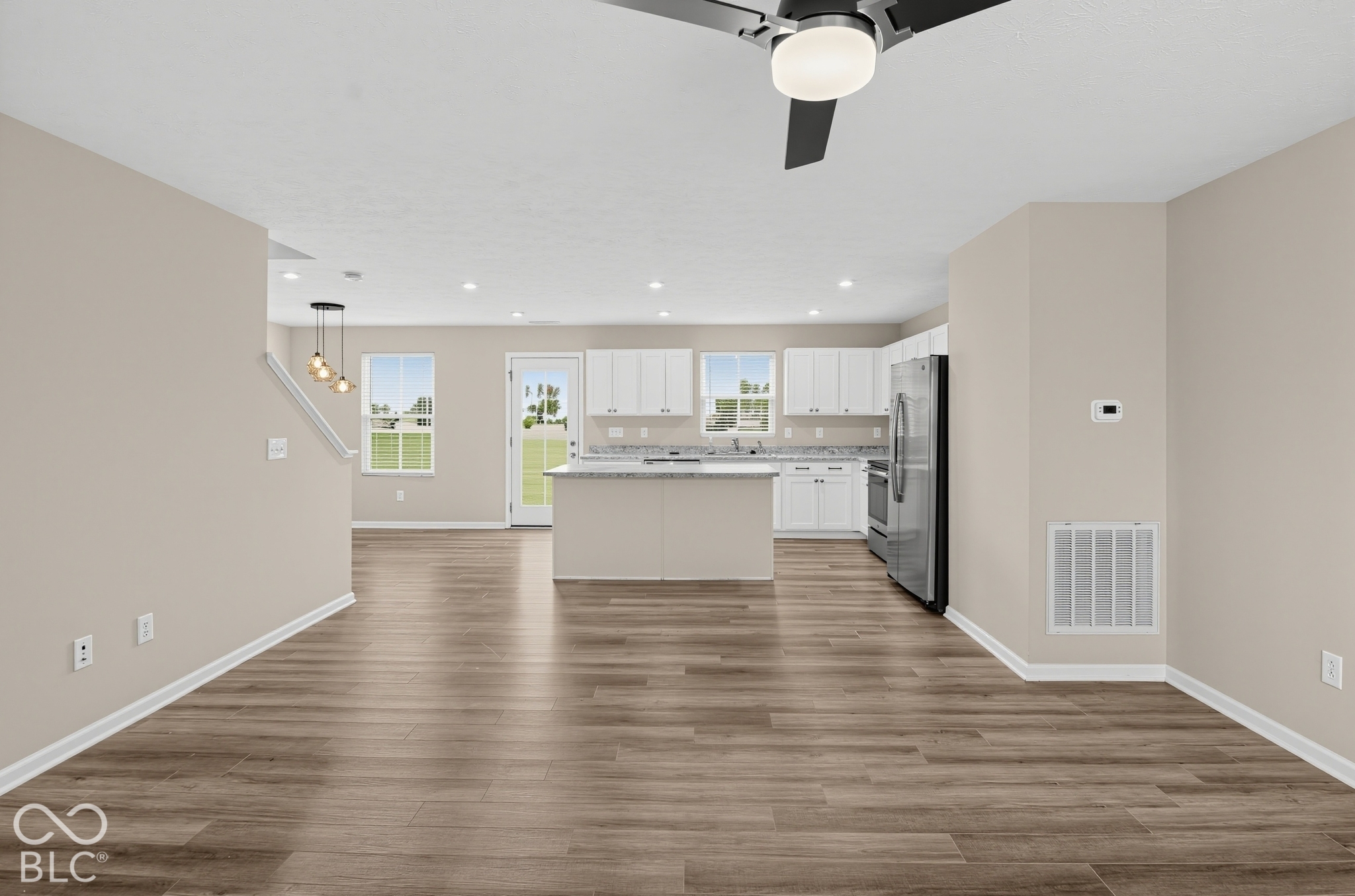 Open concept area featuring wood-finish flooring, white cabinetry, a kitchen island with stone-finish countertops, recessed lighting, and a modern ceiling fan