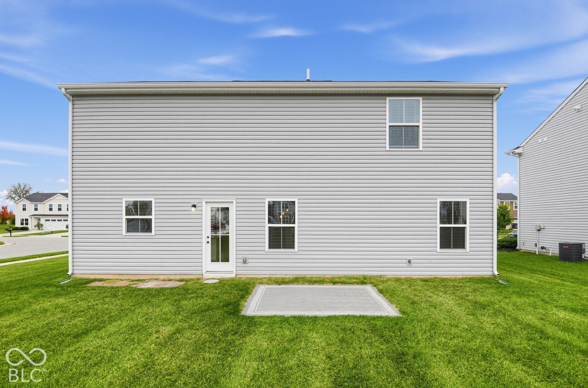 Rear exterior featuring light grey horizontal siding, four glass-paneled windows, a single-lite exterior door, and a concrete patio