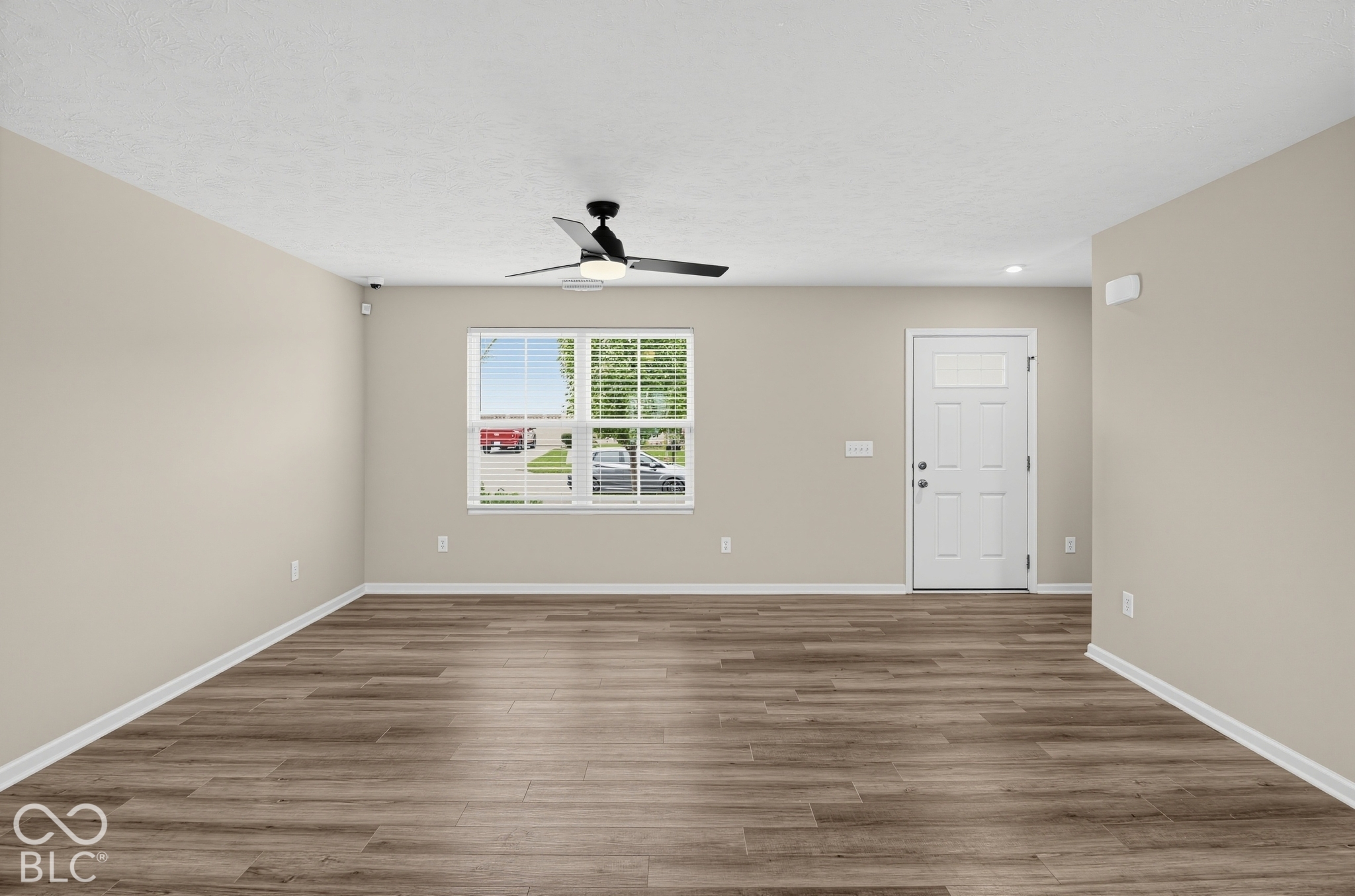 Interior space featuring wood-finish flooring, a matte black ceiling fan with integrated lighting, neutral wall paint, and an exterior door with a window inset