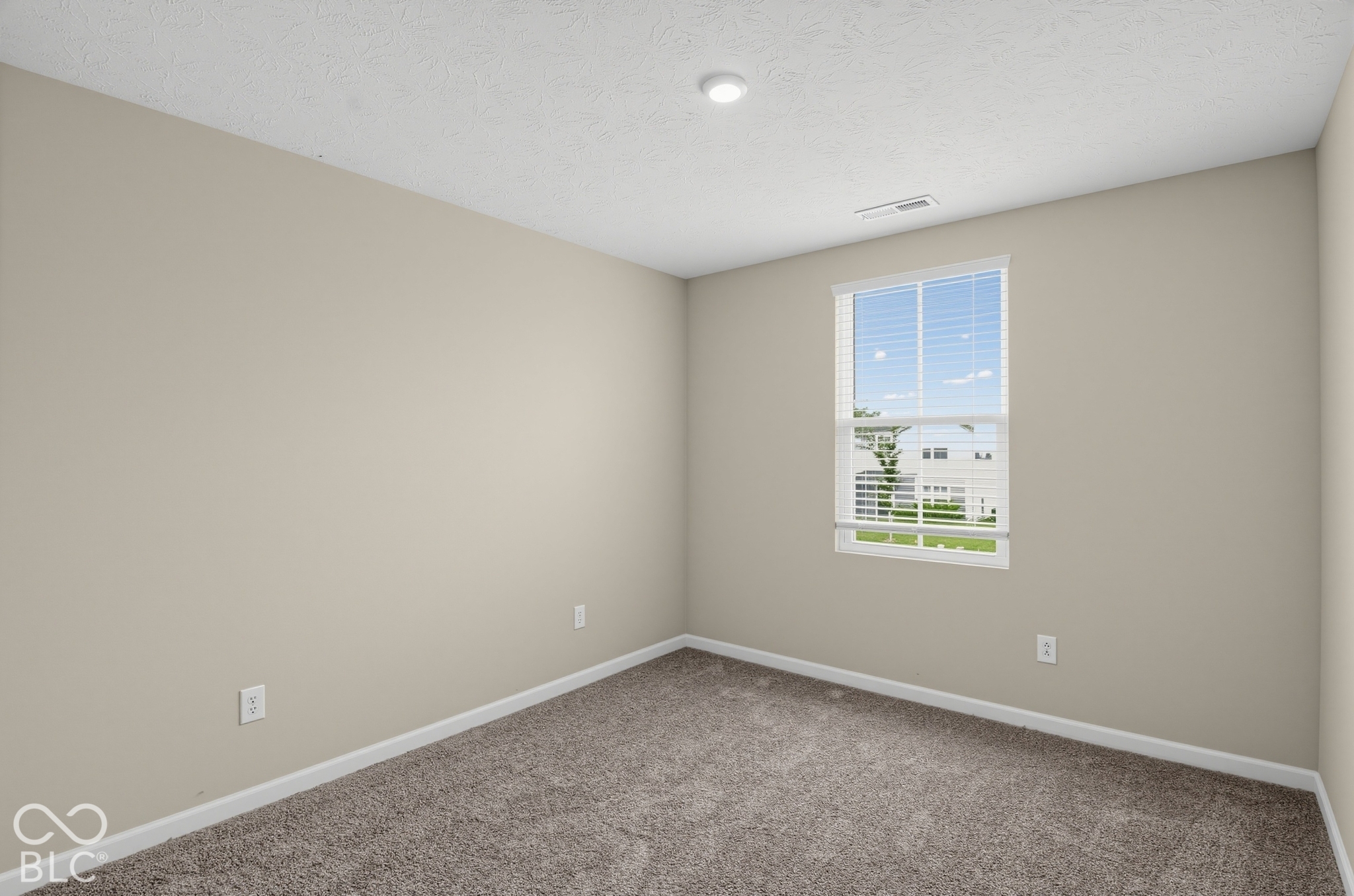Neutral-toned interior space featuring textured carpeting, neutral wall paint, and a single-pane window with integrated blinds