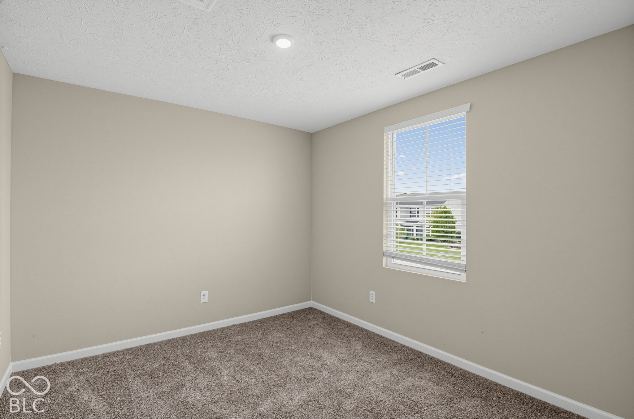 Neutral interior space featuring neutral wall tones, textured carpeting, and a single-hung window with integrated blinds