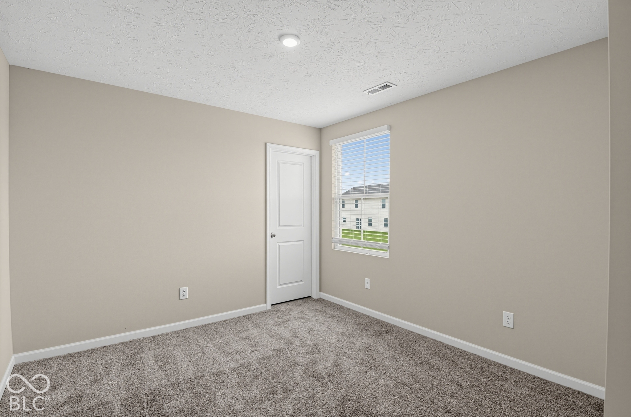 Neutral-toned interior featuring wall-to-wall carpeting, textured ceiling finish, and a single-panel interior door