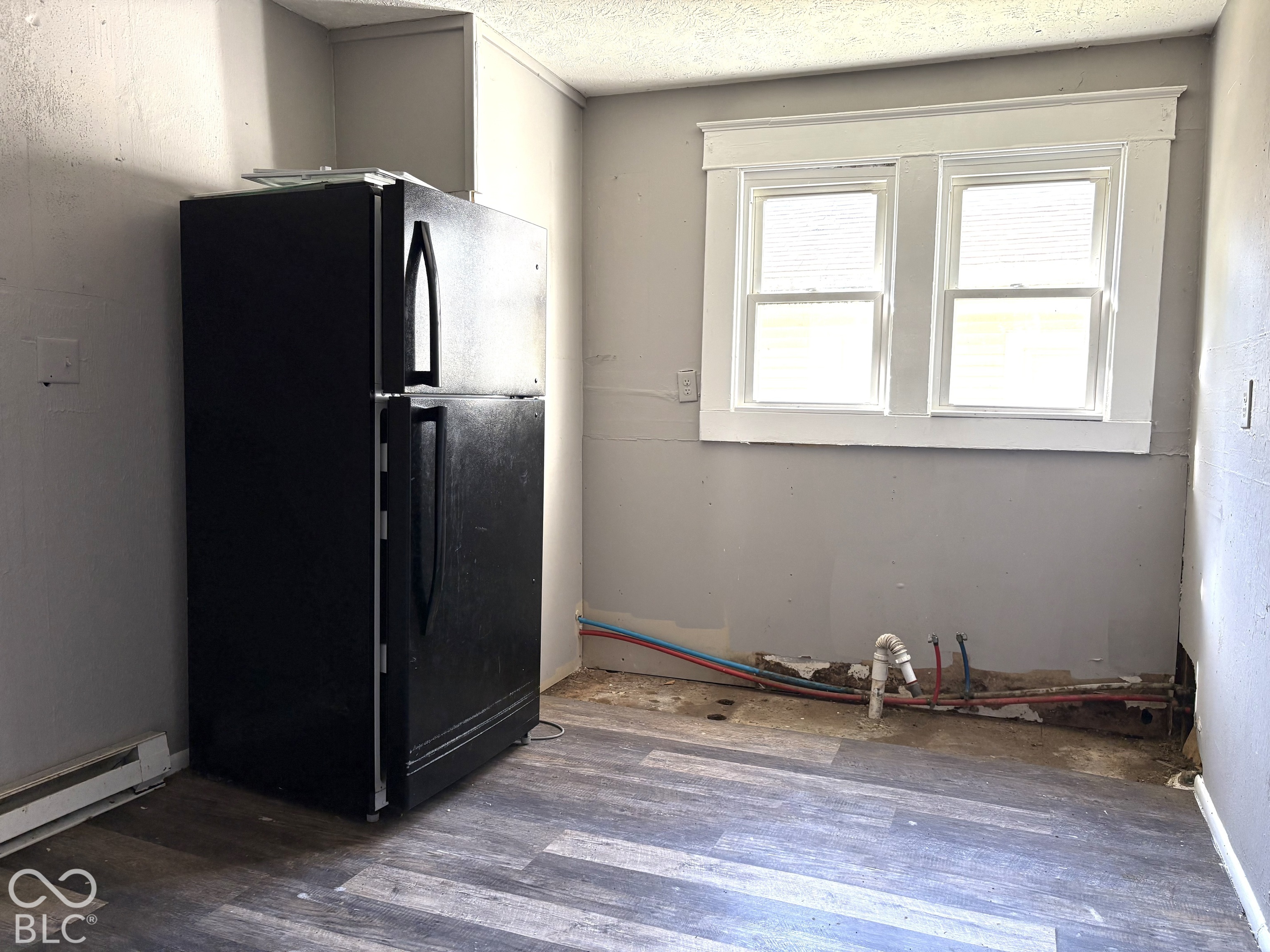 Wood-finish flooring, black top-mount refrigerator, and dual-pane window with white wood-trim casing