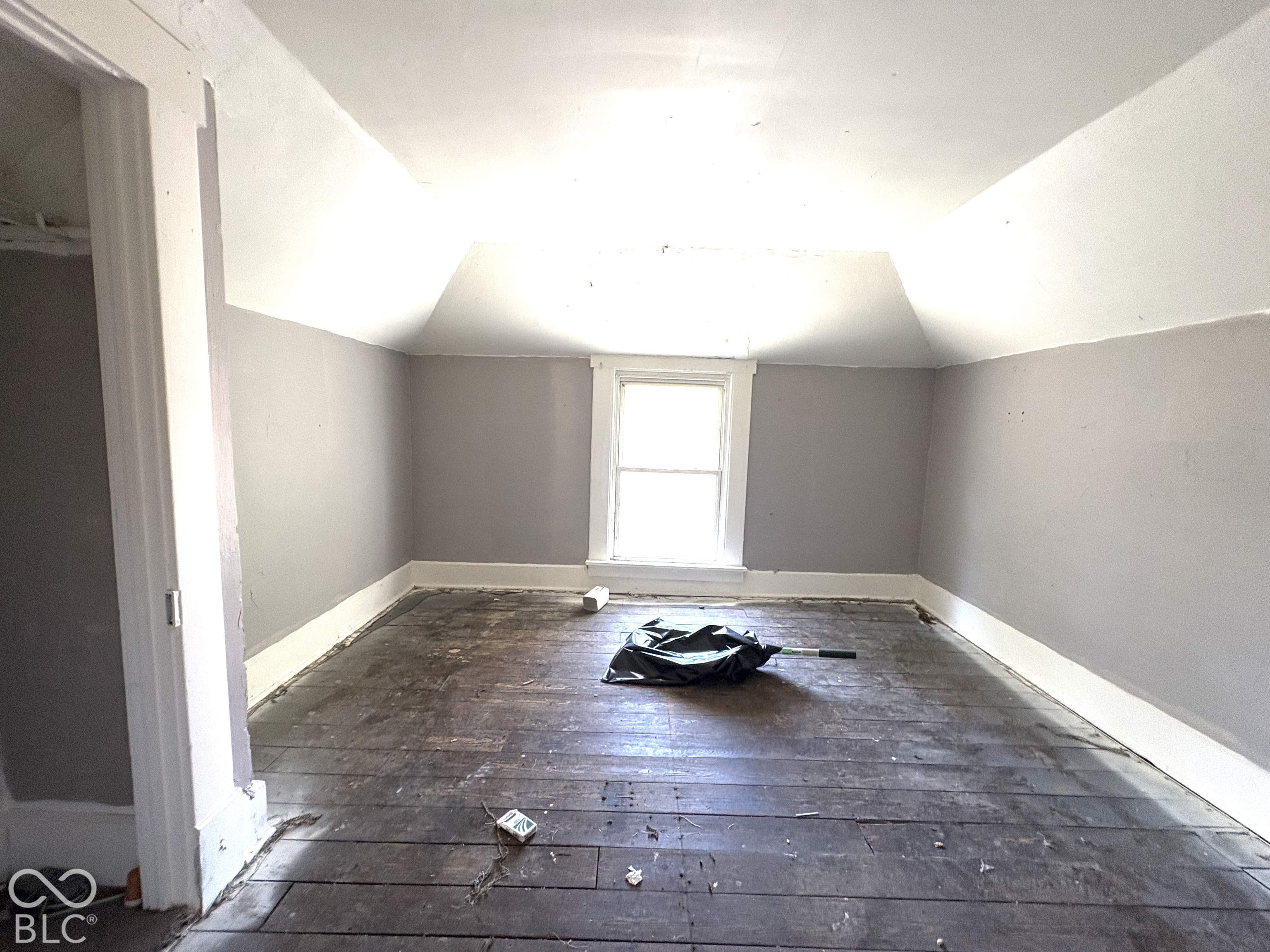 Interior space featuring vaulted ceilings, a central window with white millwork, and exposed wood plank flooring