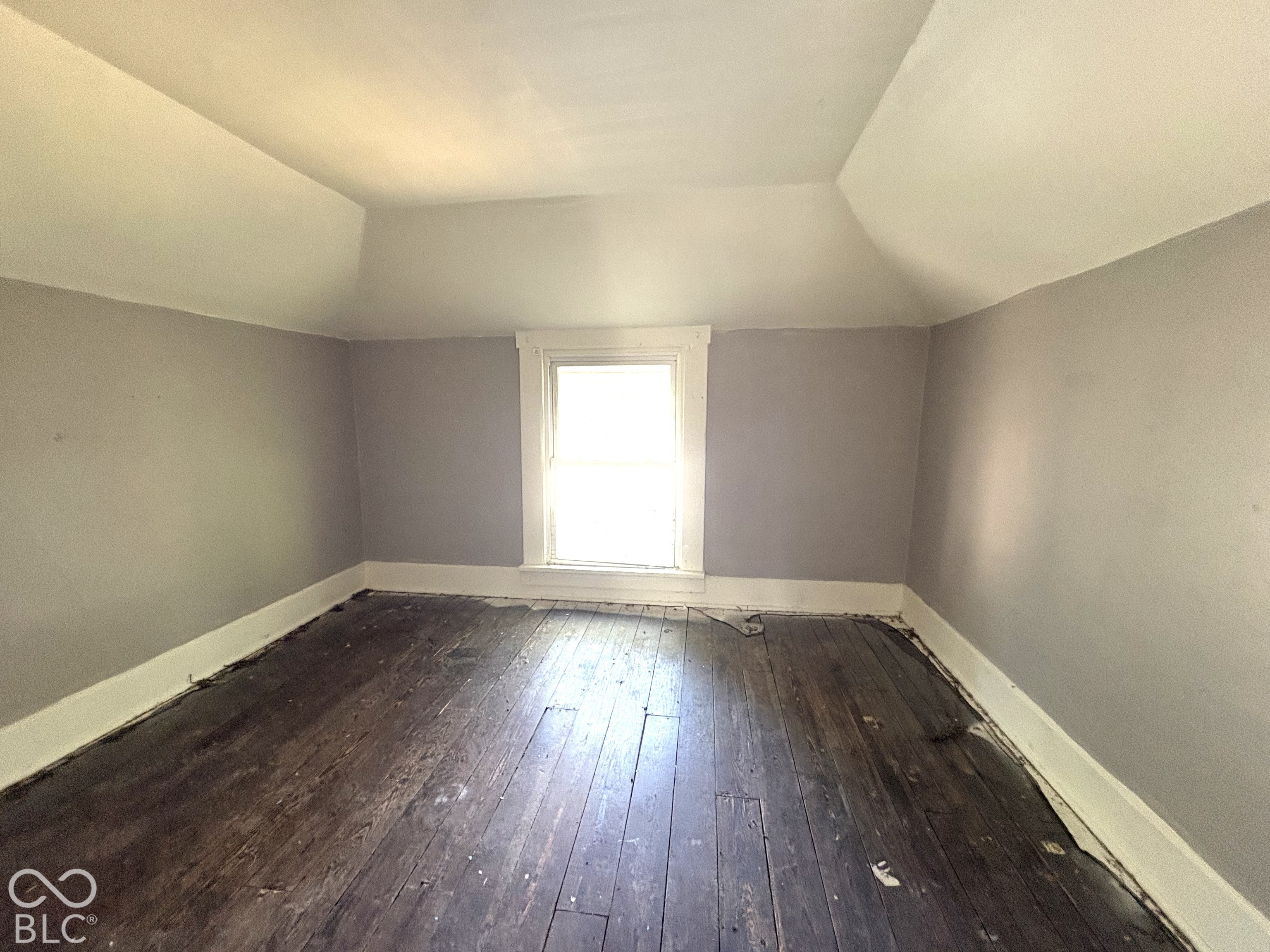 Interior room featuring vaulted ceilings, wide-plank wood flooring, and a single centered window with white casing