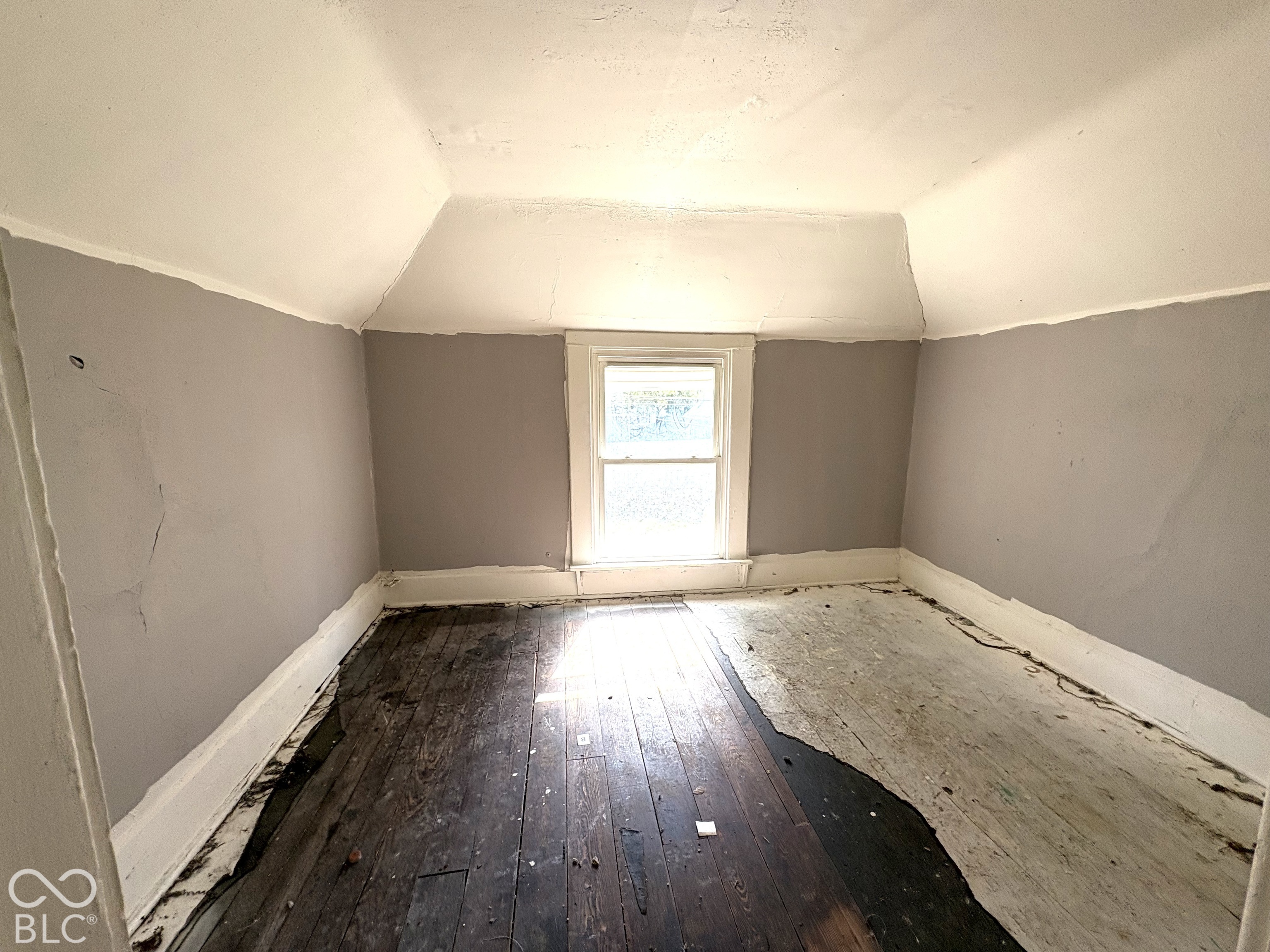 Room featuring slanted ceiling lines, wood-plank flooring, and a single centered window with white casing