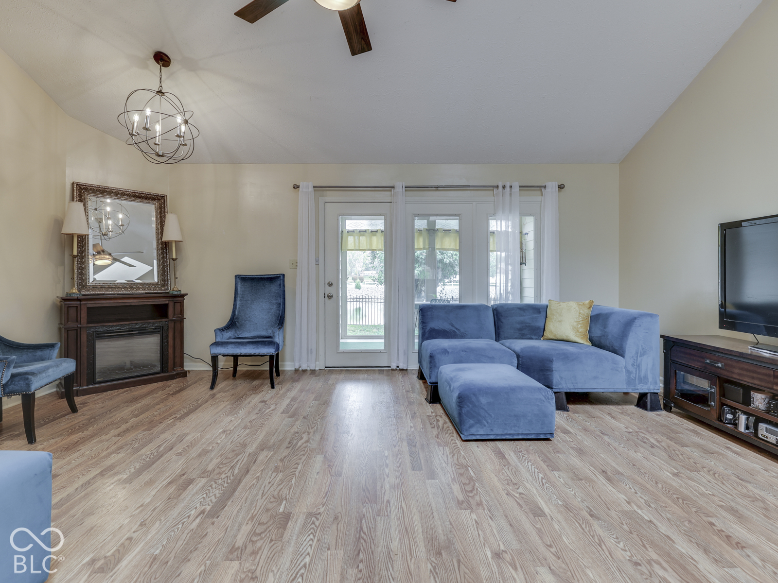 Vaulted ceilings, wood-finish flooring, built-in electric fireplace with an ornate mantel, and glass-paned exterior door with dual sidelights