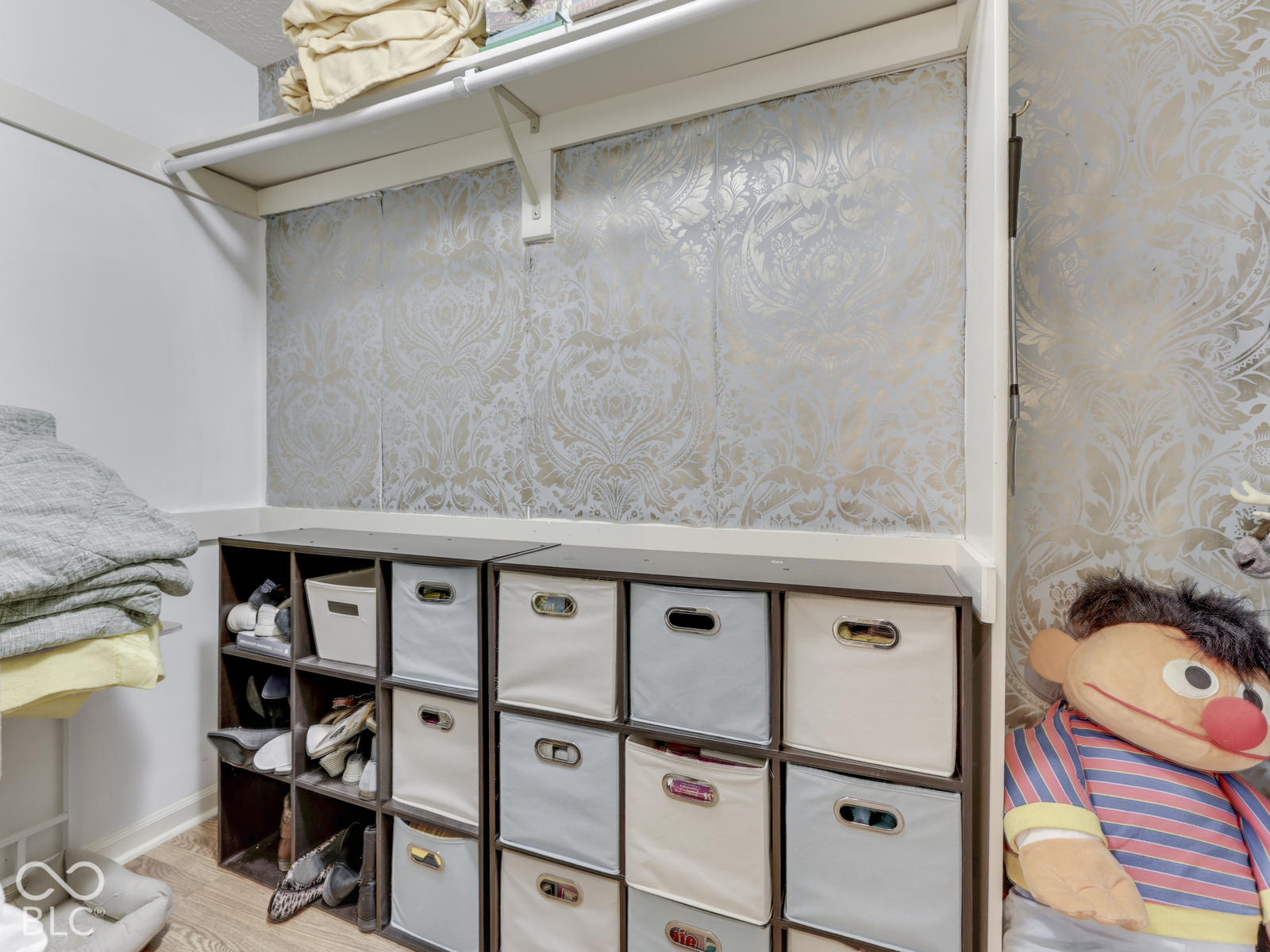 Storage closet featuring patterned wallpaper, a built-in overhead shelf, and integrated cubby shelving