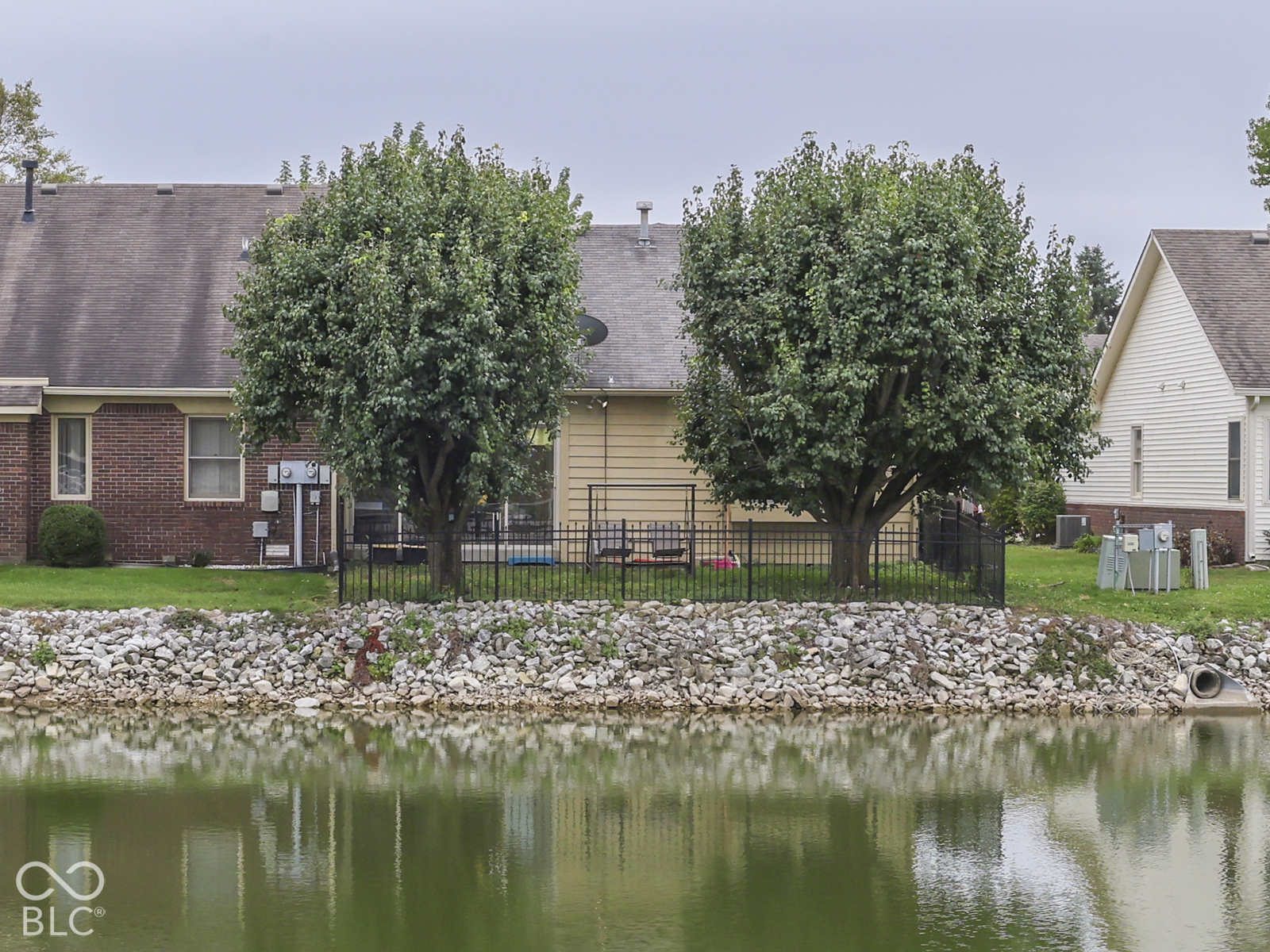 Waterfront property featuring a stone-lined bulkhead, a perimeter wrought iron fence, and mature ornamental trees