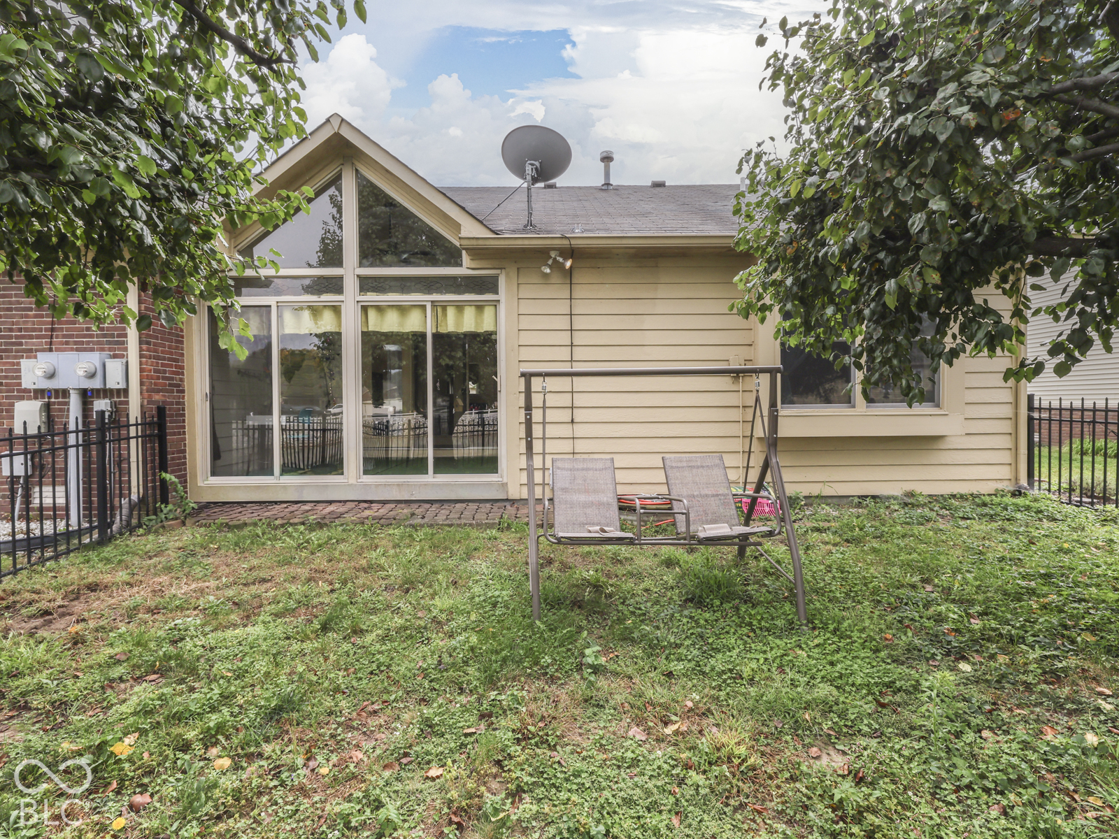 Exterior rear elevation featuring lap siding, an A-frame glass wall, brick masonry accents, a brick patio, and black metal fencing