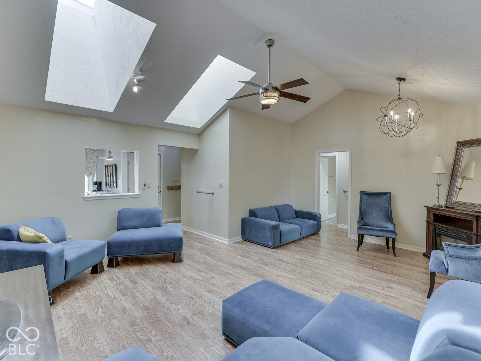 Vaulted ceiling featuring dual skylights, wood-finish flooring, a multi-blade ceiling fan, and a spherical metal chandelier