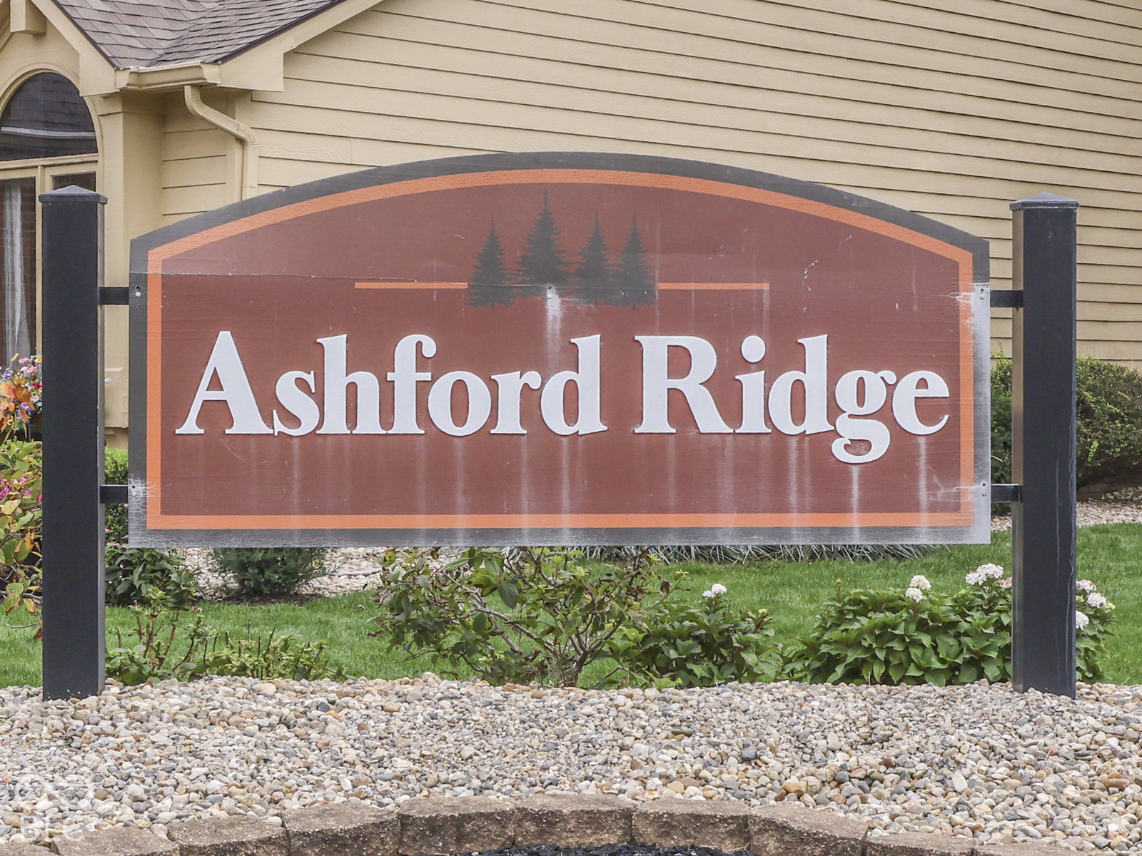 Freestanding Ashford Ridge monument signage featuring a brown panel, metal frame, and stone-bordered landscaping