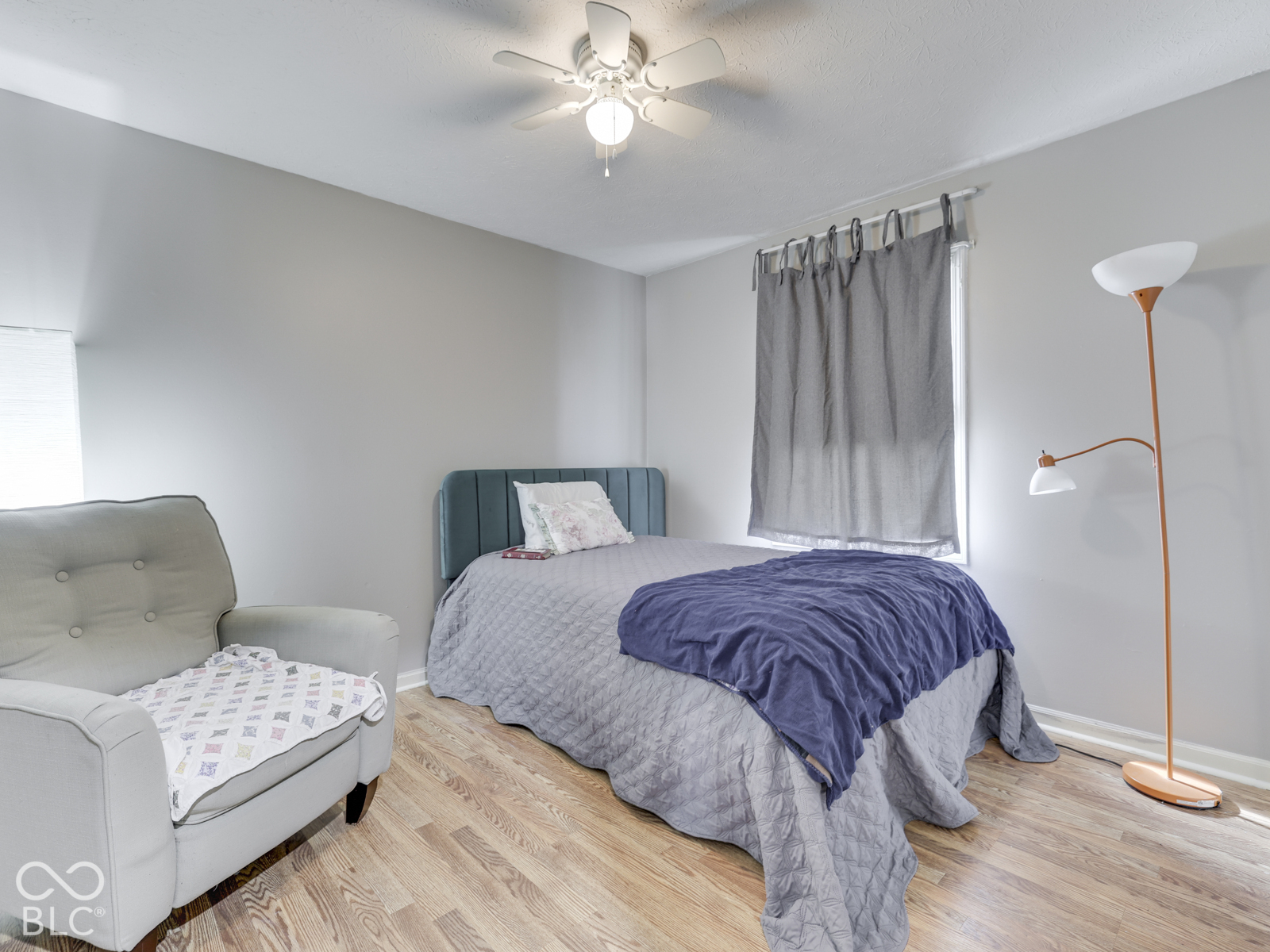 Room featuring wood-finish flooring, neutral wall paint, and a ceiling-mounted light fixture with a multi-blade fan