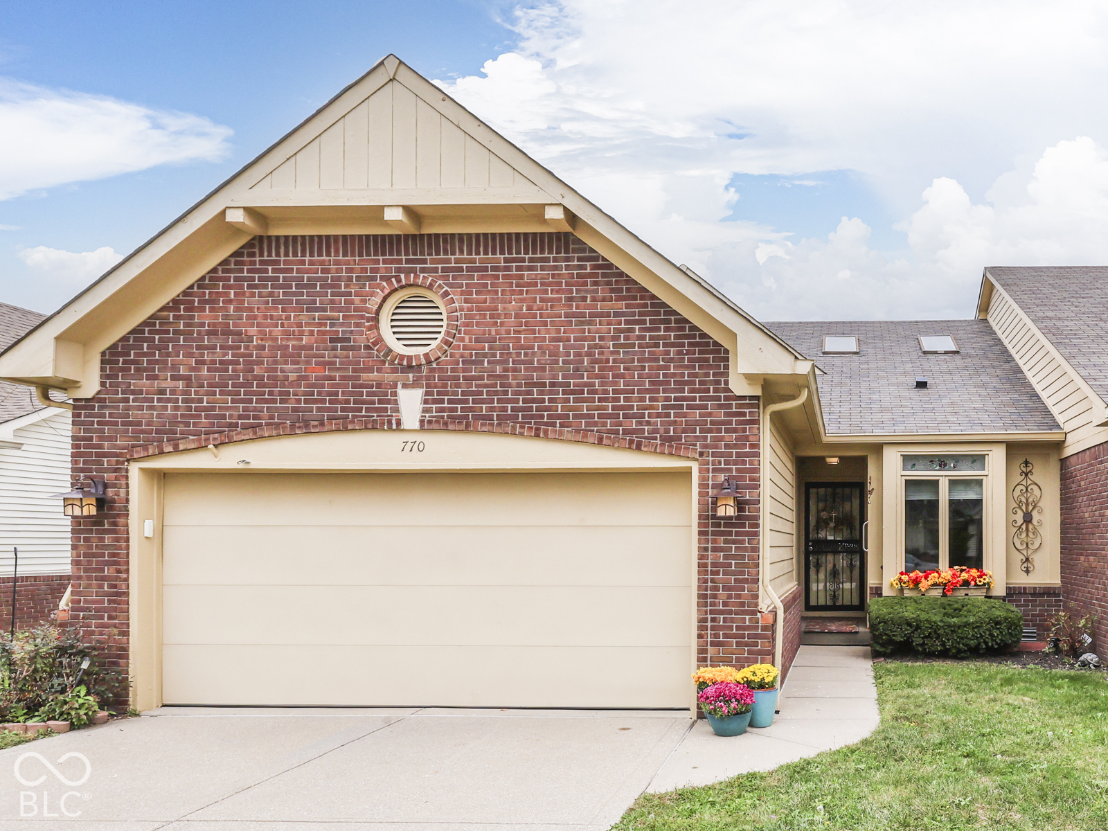 Brick exterior featuring a gabled roofline, arched garage entry, circular louvered vent, and skylights