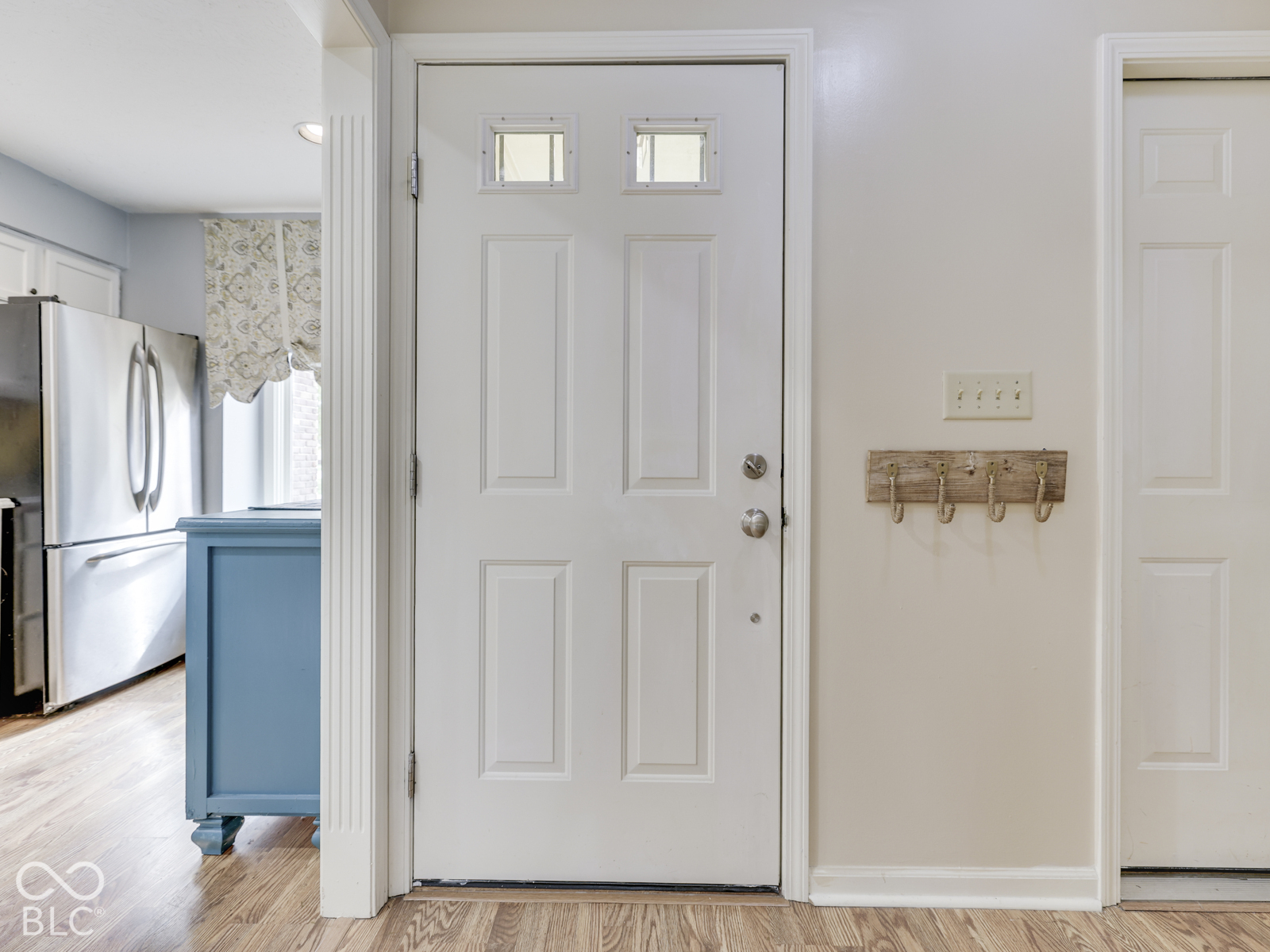 White four-panel entry door featuring two rectangular glass panes, vertical fluted trim casing, and light-toned wood-finish flooring